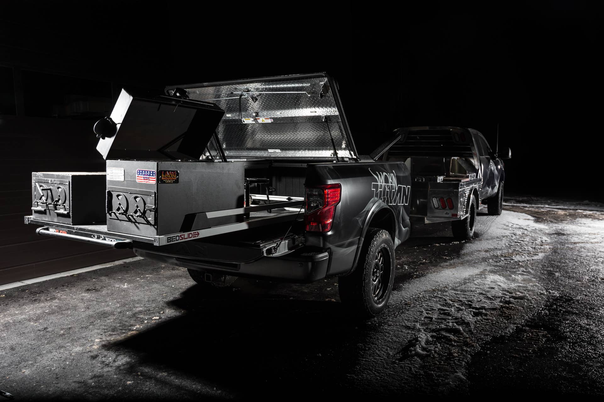 The heart of Smokinâ TITAN lies inside the custom trailer behind the truck. Since food smoking can create heat up to 600 degrees, the TITAN XDâs factory bed was removed from the truck and put on a B&S Custom trailer to prevent that heat from affecting the truck. The bed-trailer features two Nissan TITAN Boxes as lockable dry storage for the smoker pellets and wood chips flanking the smoker. Utilizing the TITANâs innovative Utili-Track System, a B&S Customizing sliding tray was designed to easily slide the smoker in and out of the bed, supporting the custom Lang BBQ Smoker and Char Grill.