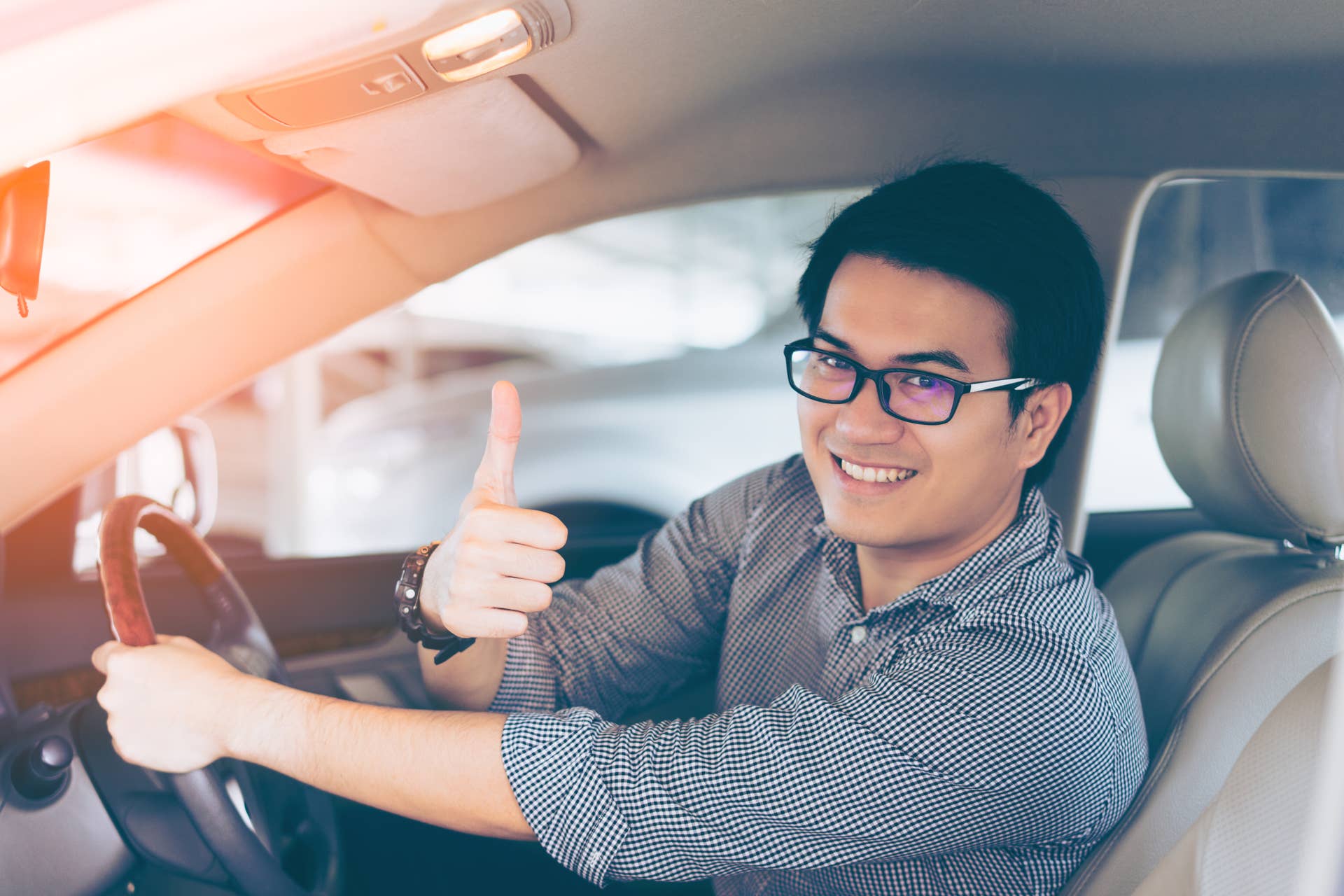 Young asian handsome man smiling and showing thumbs up in his car