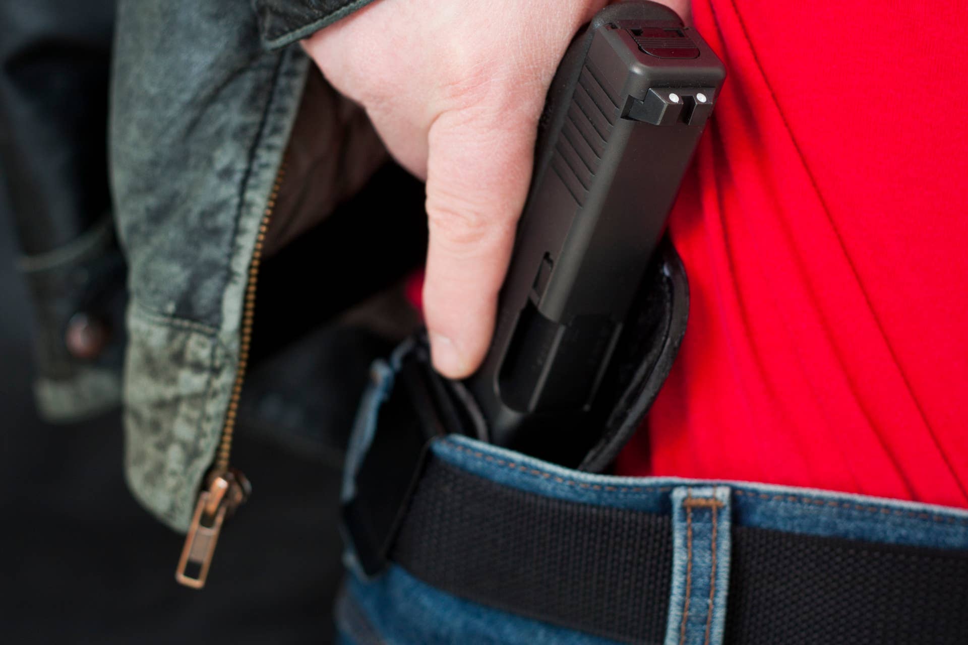 A caucasian man drawing his modern polymer (Glock) .45 caliber pistol from an IWB (inside the waistband) holster under his leather jacket. Showing proper trigger control by keeping his finger off the trigger as he draws.All images in this series...