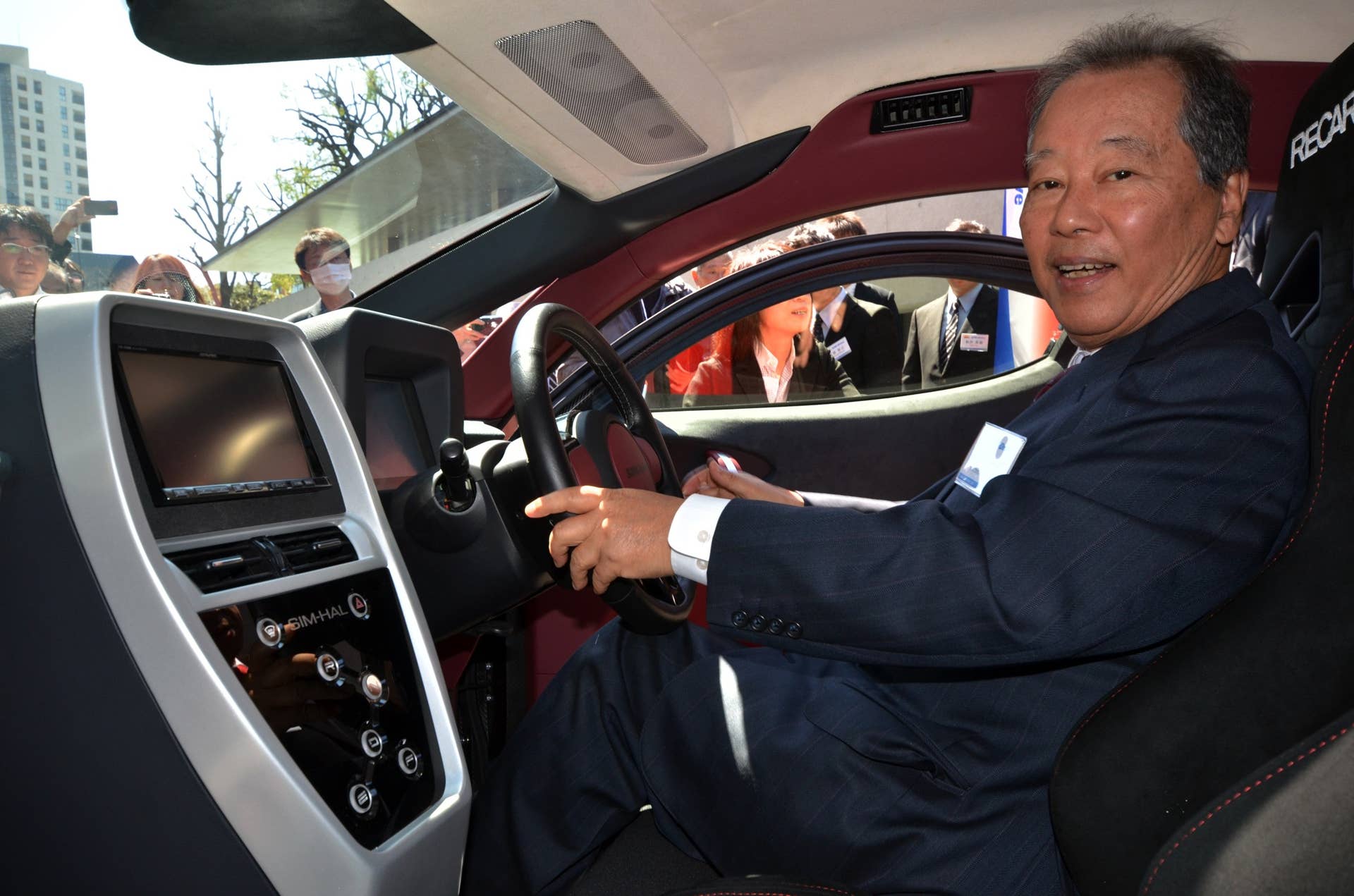 Japan's electric vehicle venture SIM-Drive chairman Soichiro Fukutake (L) smiles as he sits inside the fourth generation model of the company's electric vehicle 'SIM-HAL' at the University of Tokyo on March 31, 2014. SIM-HAL has newly developed highly efficient in-wheel motors for all wheels and enables a drive of 400km with a charge.   AFP PHOTO / Yoshikazu TSUNO        (Photo credit should read YOSHIKAZU TSUNO/AFP/Getty Images)