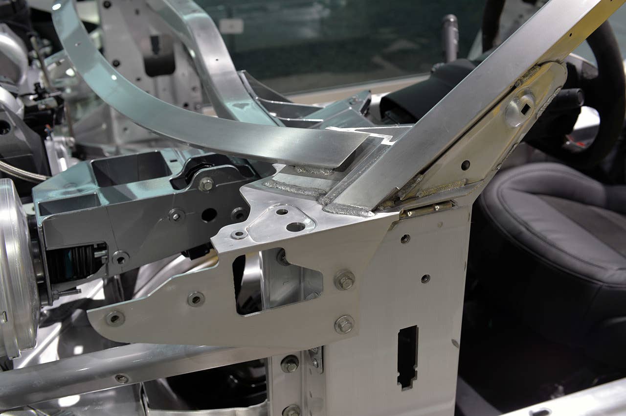 The base of the windshield, or A-pillar, is a combination of aluminum alloys. The components are welded and bolted into place, with gussets to reinforce and reduce stress on the complex joints. The darker gray piece, to the left of the image, is the mounting bracket for the braking system's master cylinder.