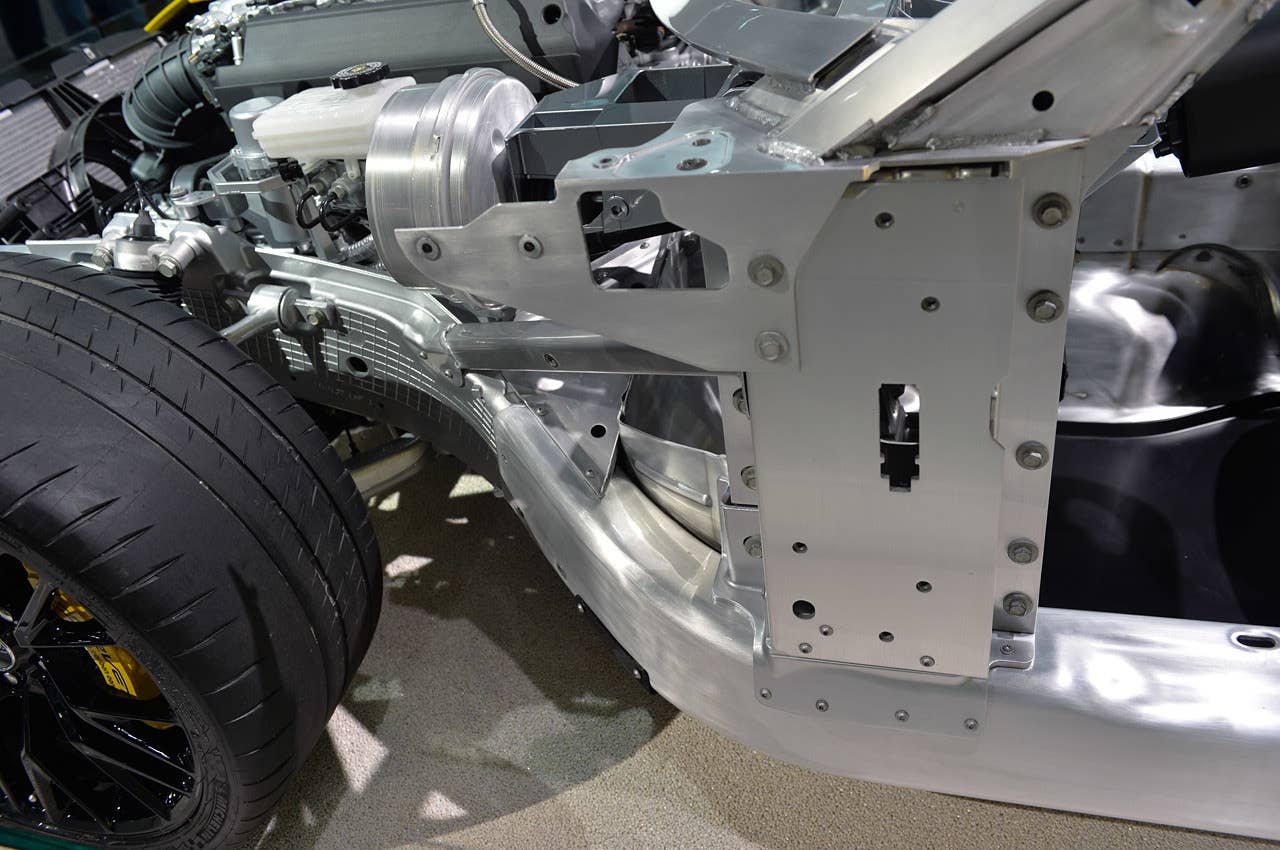 This is a great view of the left front quarter panel, clearly showing the cast aluminum component (it has gridded lines on it) containing the suspension mounting points. The curved frame rail at the bottom is hydroformed aluminum, while the aluminum above is sheet that has been cut. The silver drum is the master cylinder, with a clear brake fluid reservoir on its top. Note the sticky Michelin tires.