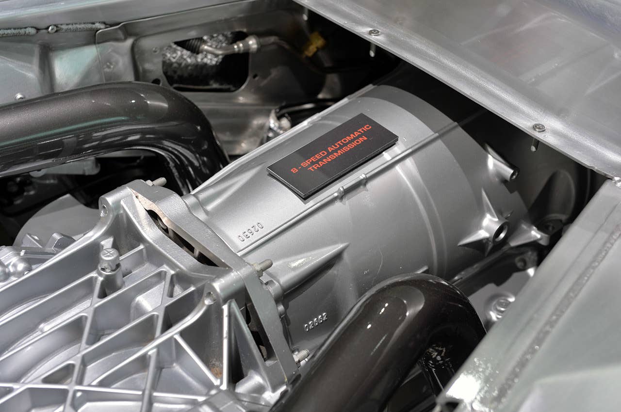 The eight-speed automatic transmission is flanked by steel tubes carrying hot exhaust to the rear mufflers. The finned aluminum differential casing is on the lower left of the frame.