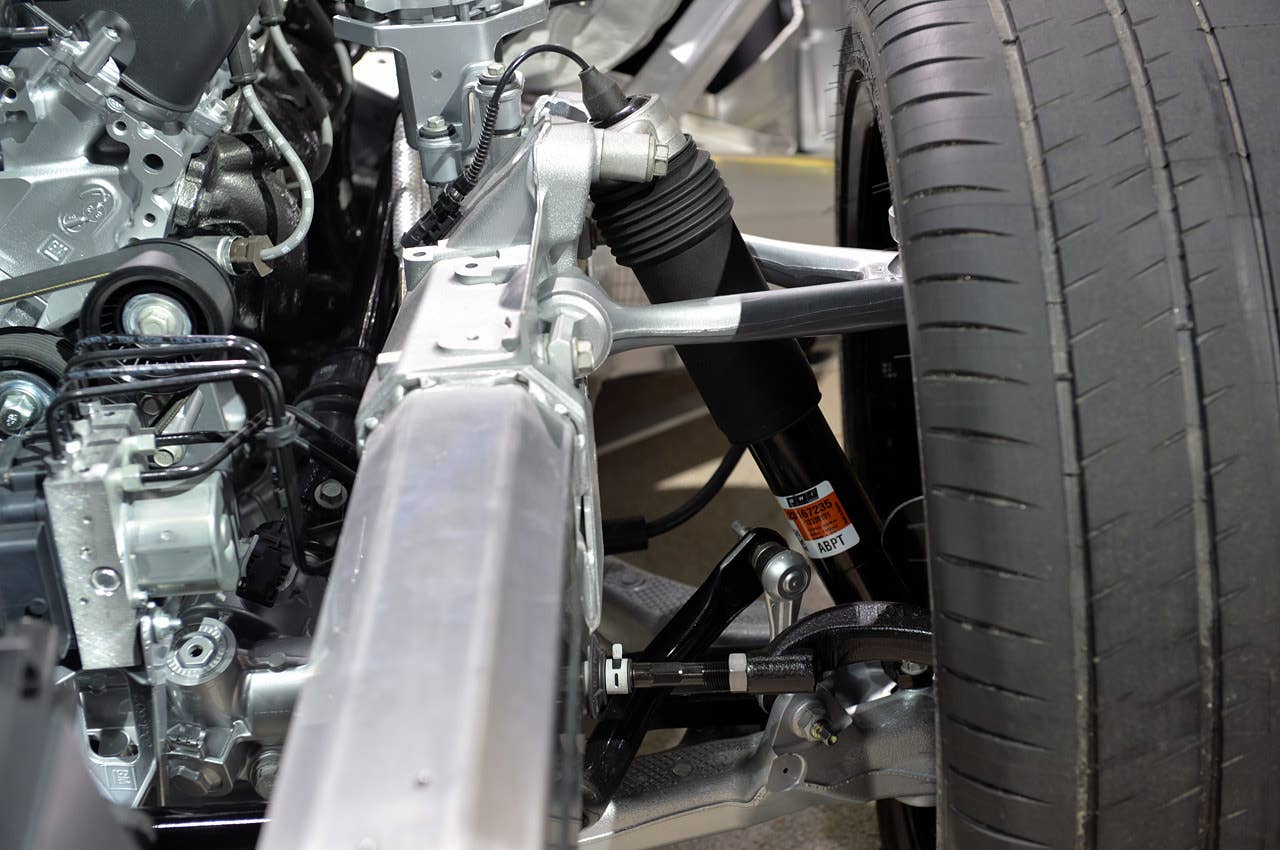 Looking towards the front left wheel from the front of the Z06, the aluminum double-wishbone suspension is in plain sight (Chevrolet calls it a Short/Long Arm, or SLA, suspension). The large black cylinder, running down at an angle, is the magnetorheological damper that is part of the adaptive control suspension system. While the anti-roll bar (in black) is visible, it is nearly impossible to see the transverse composite leaf spring pressing against the lower control arm.