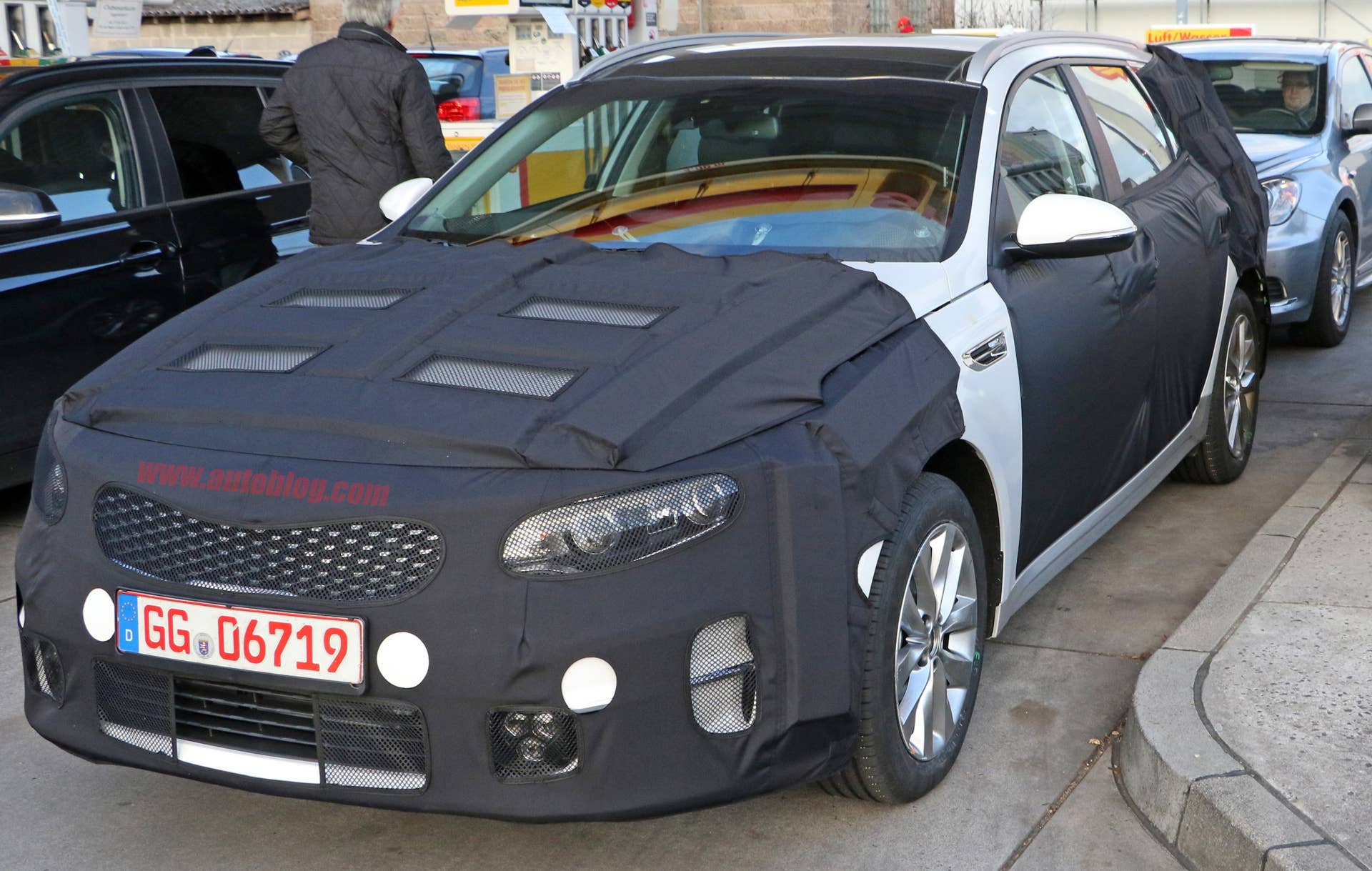 Kia Sportswagon prototype caught by spy photographers, front three-quarter at a gas station.