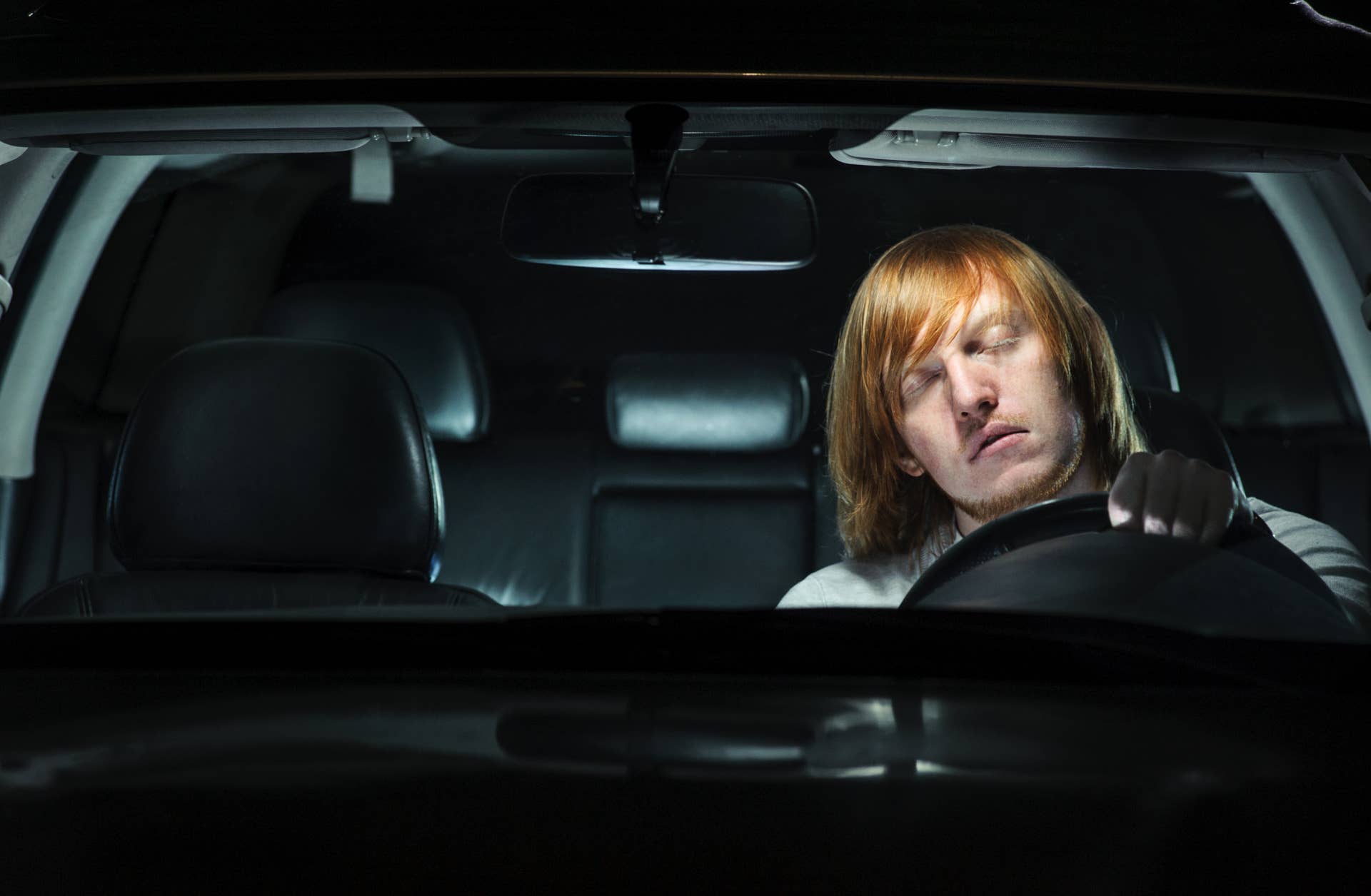 A young man exhausted and falling asleep while driving his car at night