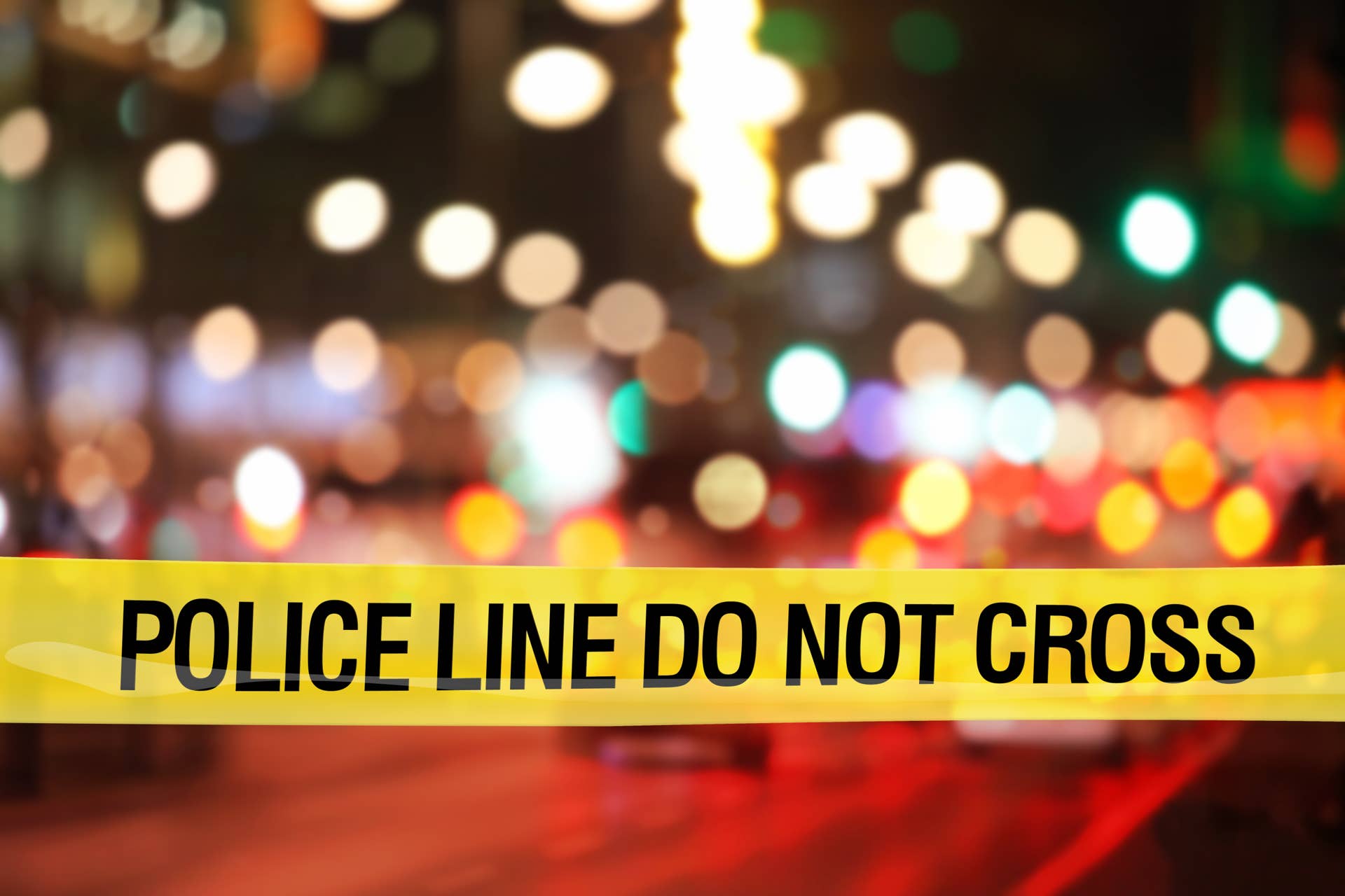 'Police line do not cross' yellow plastic tape marks the boundary to a restricted area in a city downtown at night with street light, where police forces are investigating crimes or accidents and performing their duties. Outdoor crime scene. Defocused background. Copy space on image top side.