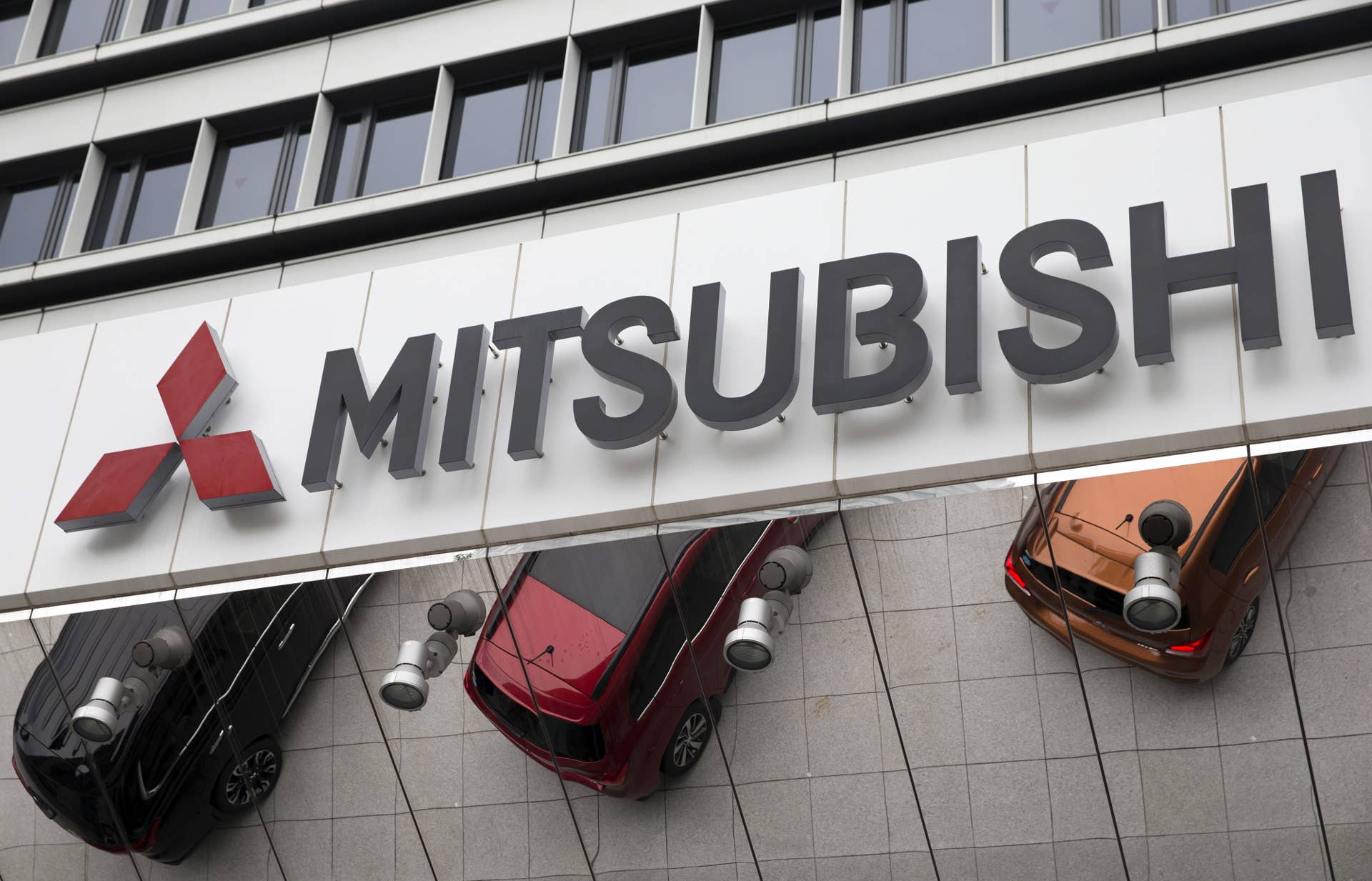 Mitsubishi Motors Corp. vehicles are reflected under a sign outside the company's headquarters in Tokyo, Japan, on Tuesday, Aug. 2, 2016. An investigation of practices at Mitsubishi Motors found a corporate culture where workers couldn't push back against management demands, contributing to the fuel-economy manipulation scandal that's pushed the Japanese carmaker to seek a rescue from Nissan Motor Co. Photographer: Tomohiro Ohsumi/Bloomberg via Getty Images