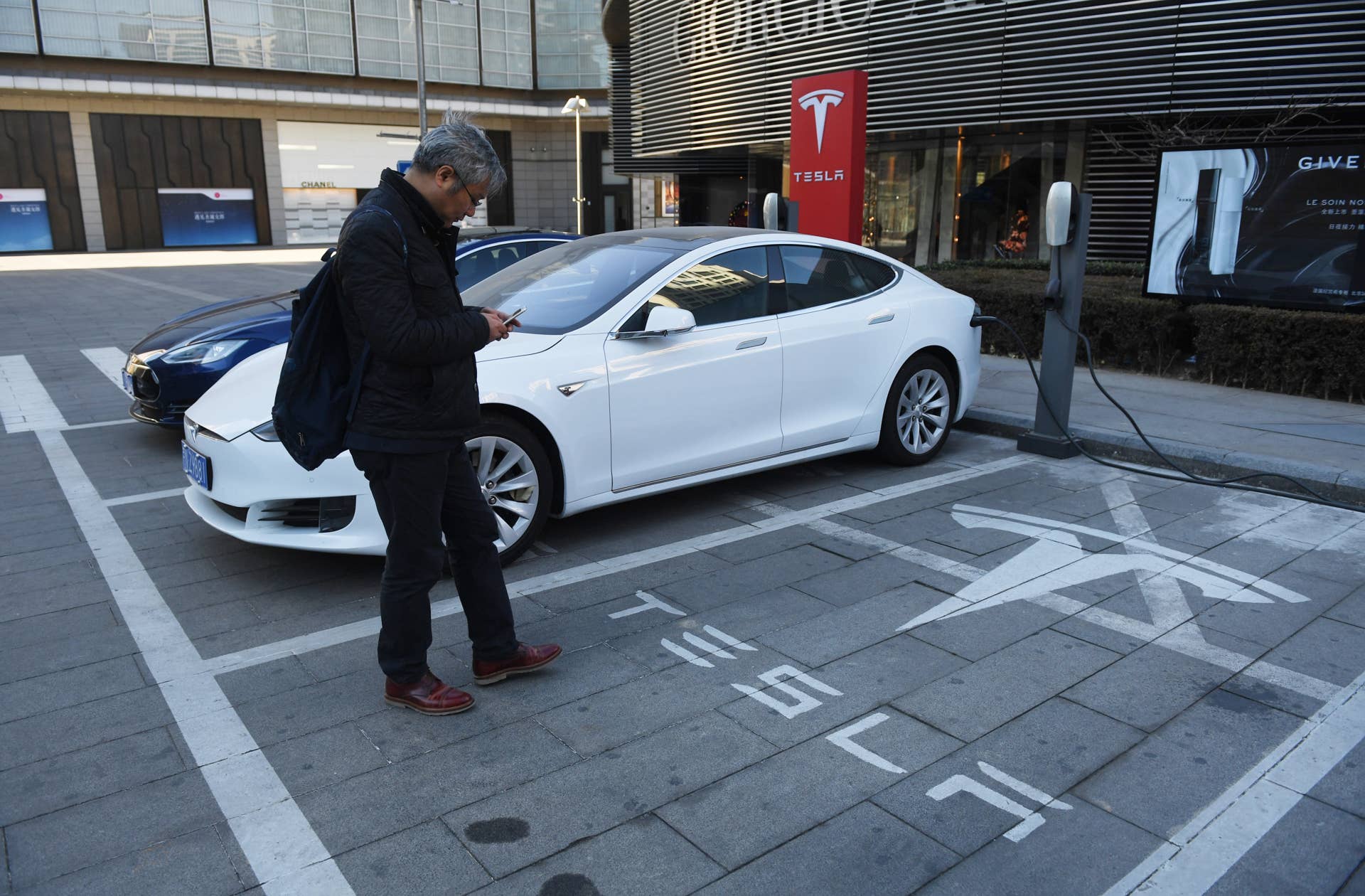 A man walks past a Tesla charging station in Beijing on December 15, 2016. Auto sales in China, the worlds biggest car market and crucial to manufacturers worldwide, reached a new peak in November, data from an industry group showed on December 12. Sales reached 2.94 million units last month, up 16.6 percent year-on-year, the the China Association of Automobile Manufacturers (CAAM) said in a statement. / AFP / GREG BAKER (Photo credit should read GREG BAKER/AFP/Getty Images)