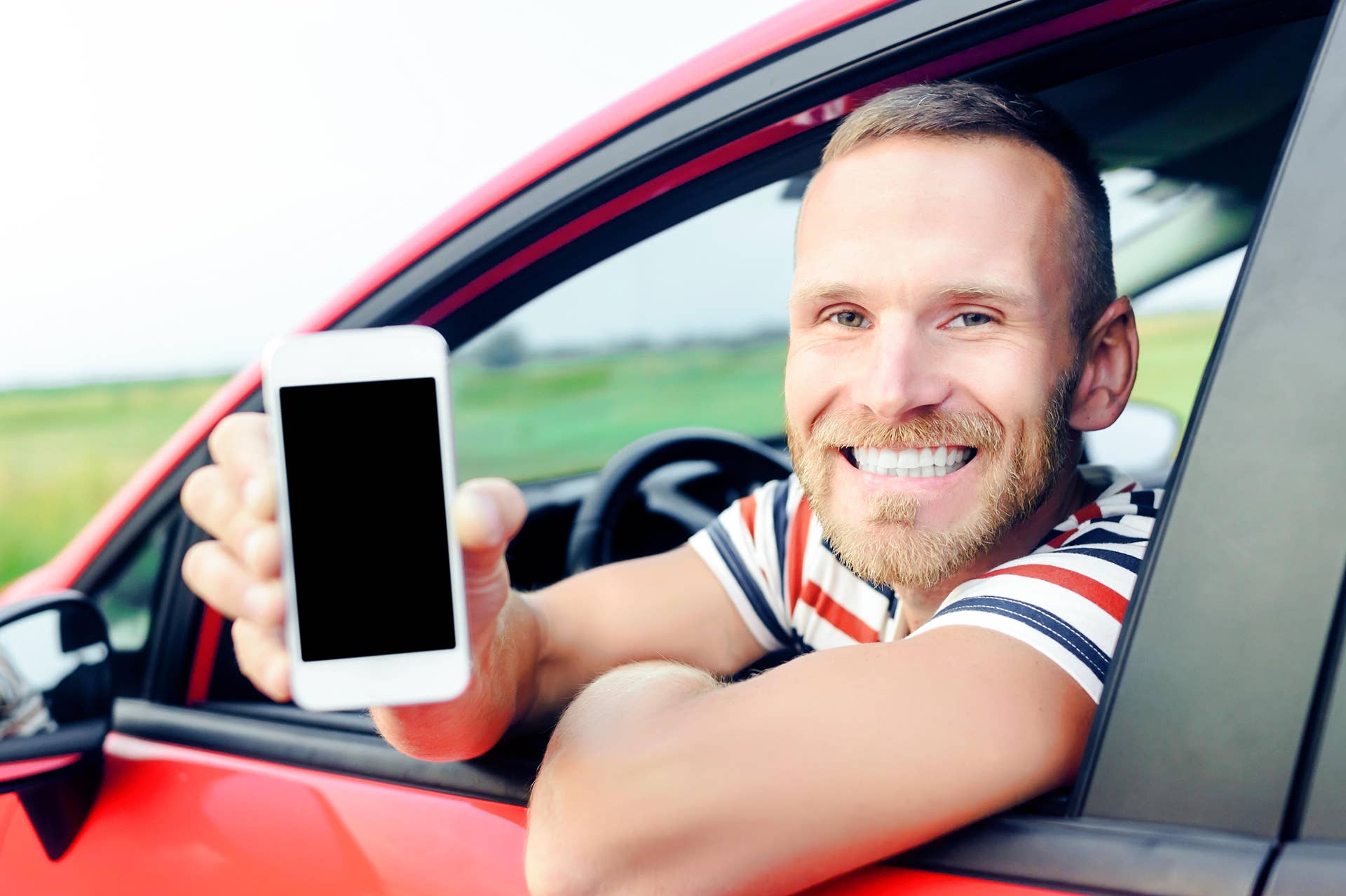 Man in car showing smart phone display smiling happy. Focus on model. Toned photo.