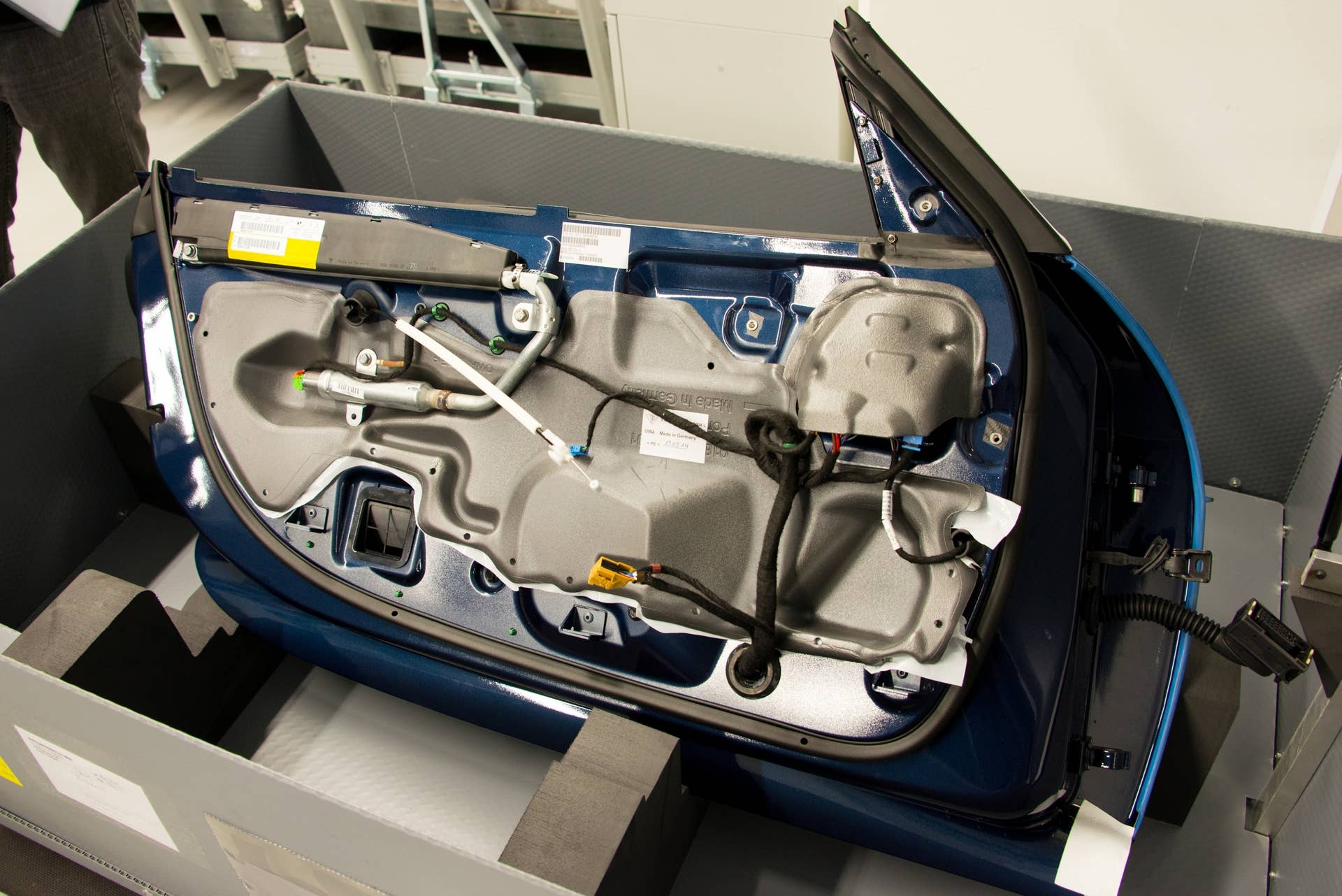 Door panels arrive in their own shipping container, painted and nearly completely assembled with the exception of interior trim (which will be hand crafted and installed during the build). Note the side airbag housing (the large black plastic rectangle just below the window sill) that has a remote pressure cylinder (the silver tube several inches below it) to optimize its packaging. The gray material is a lightweight foam used for acoustic and temperature insulation. The wires are wrapped tightly in a cloth tape.