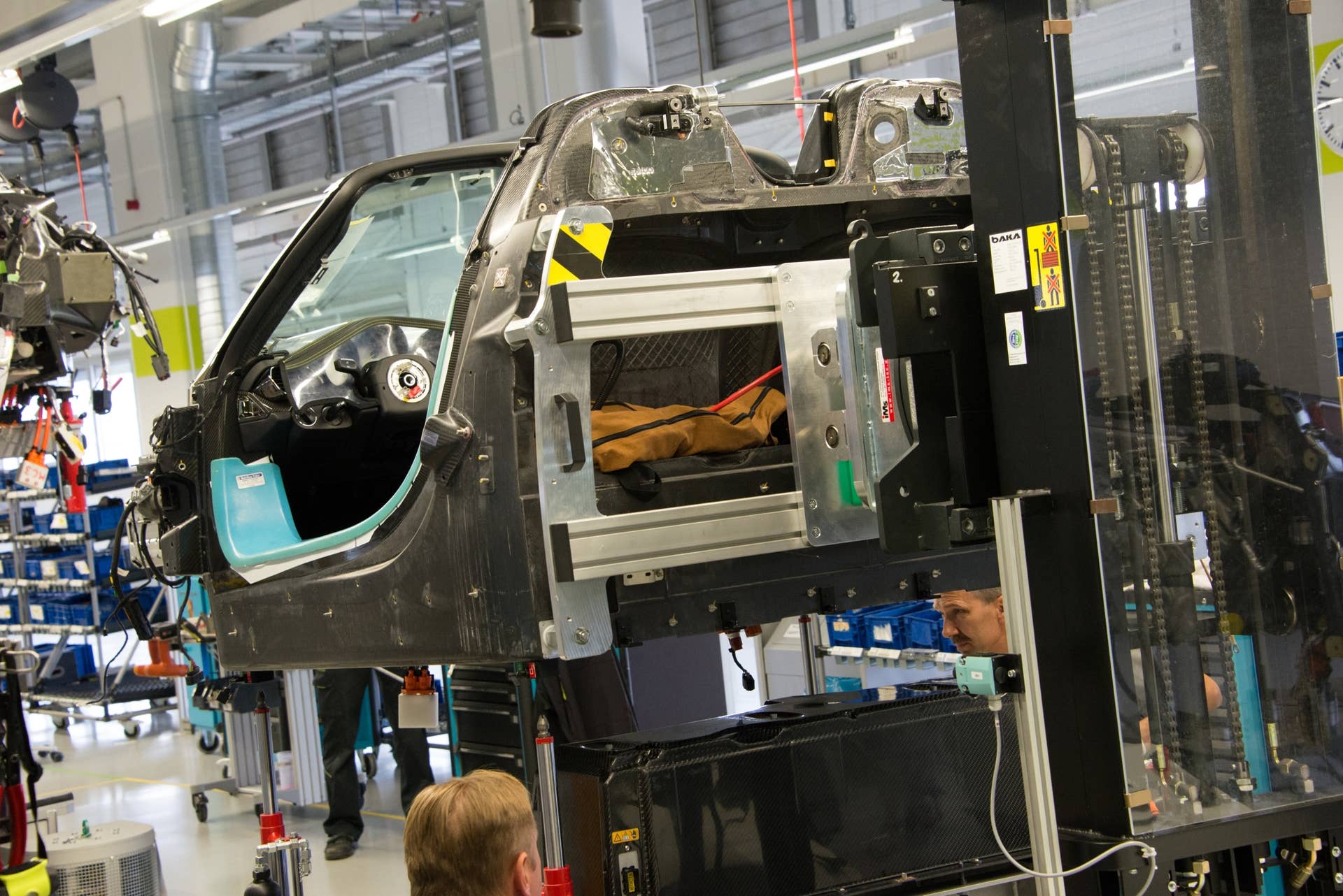 The carbon-fiber tub, with most of its primary wiring in place, is hoisted high by a forklift so the battery pack may be moved into position beneath – and slightly to the rear – of the passenger compartment. This placement keeps the center of gravity very low.  The 6.8 kWh, liquid-cooled lithium-ion battery pack, which weighs as much as the combustion engine, is completely self-contained and held in place by several bolts.