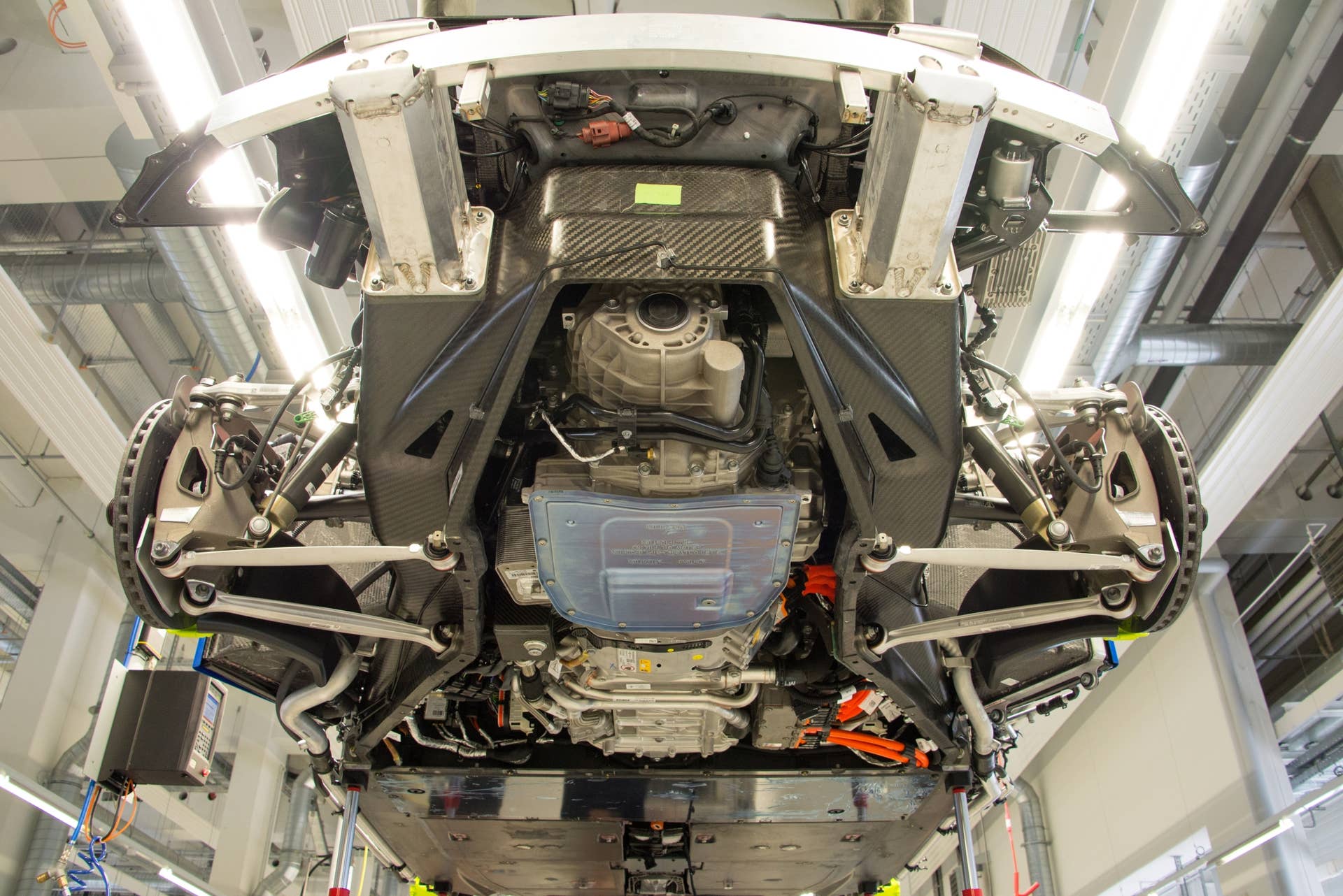 A superb view of the underside of the 918 Spyder, without its bodywork, bumper or aerodynamic lower fairing in place.  Easily viewed are the extruded aluminum beams, which are designed to crush in an accident, and the mounting points for the rear suspension. The engine's flat sump is light blue, in the center of the image.