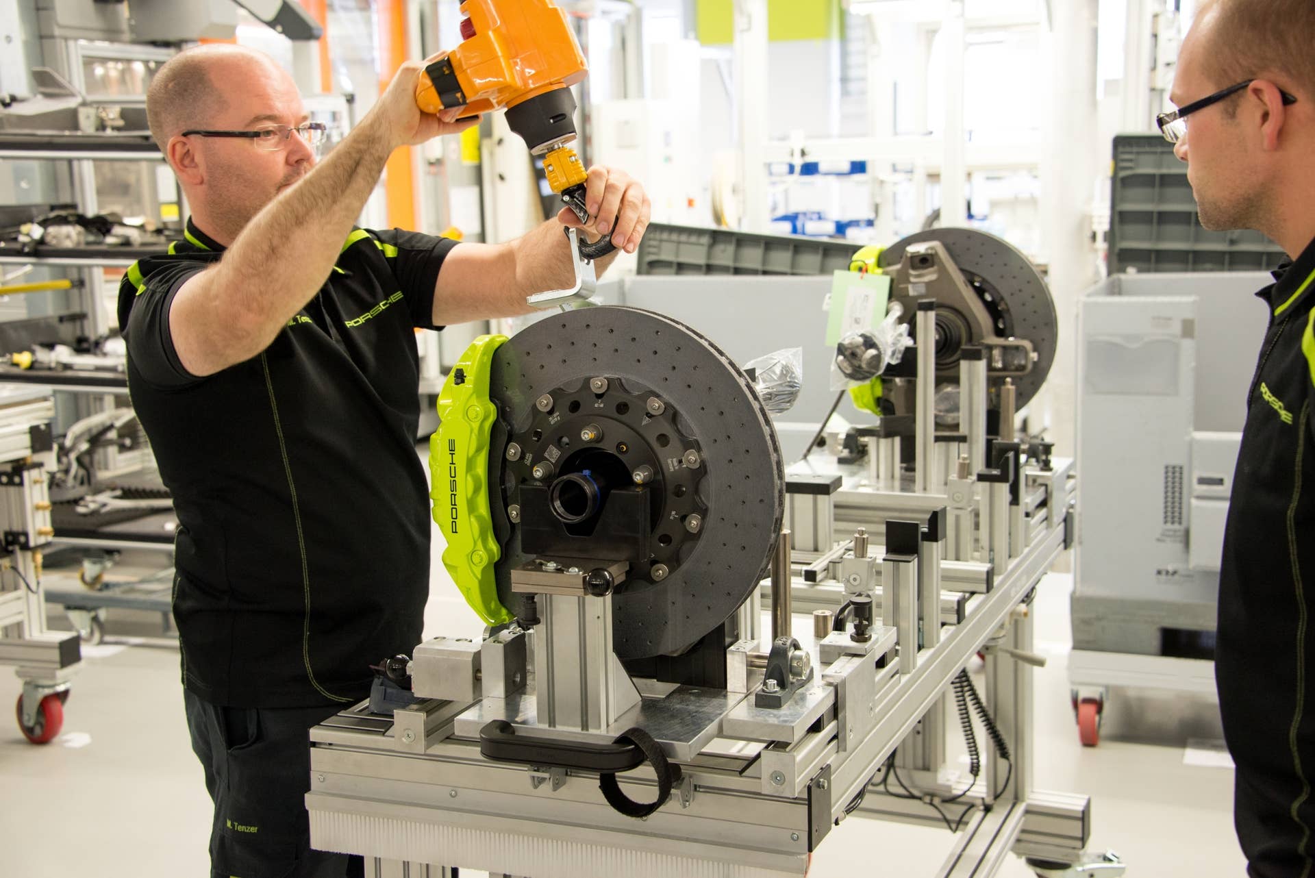 After the brake assemblies are removed from their shipping container, they are placed on a special rolling rig for inspection and adjustment before being bolted onto the tub. The brakes arrive with pads already loaded into the calipers, but without the brake lines.  In this image, the worker on the left is removing the temporary hardware that allows the electric winch to lift it from the shipping container.