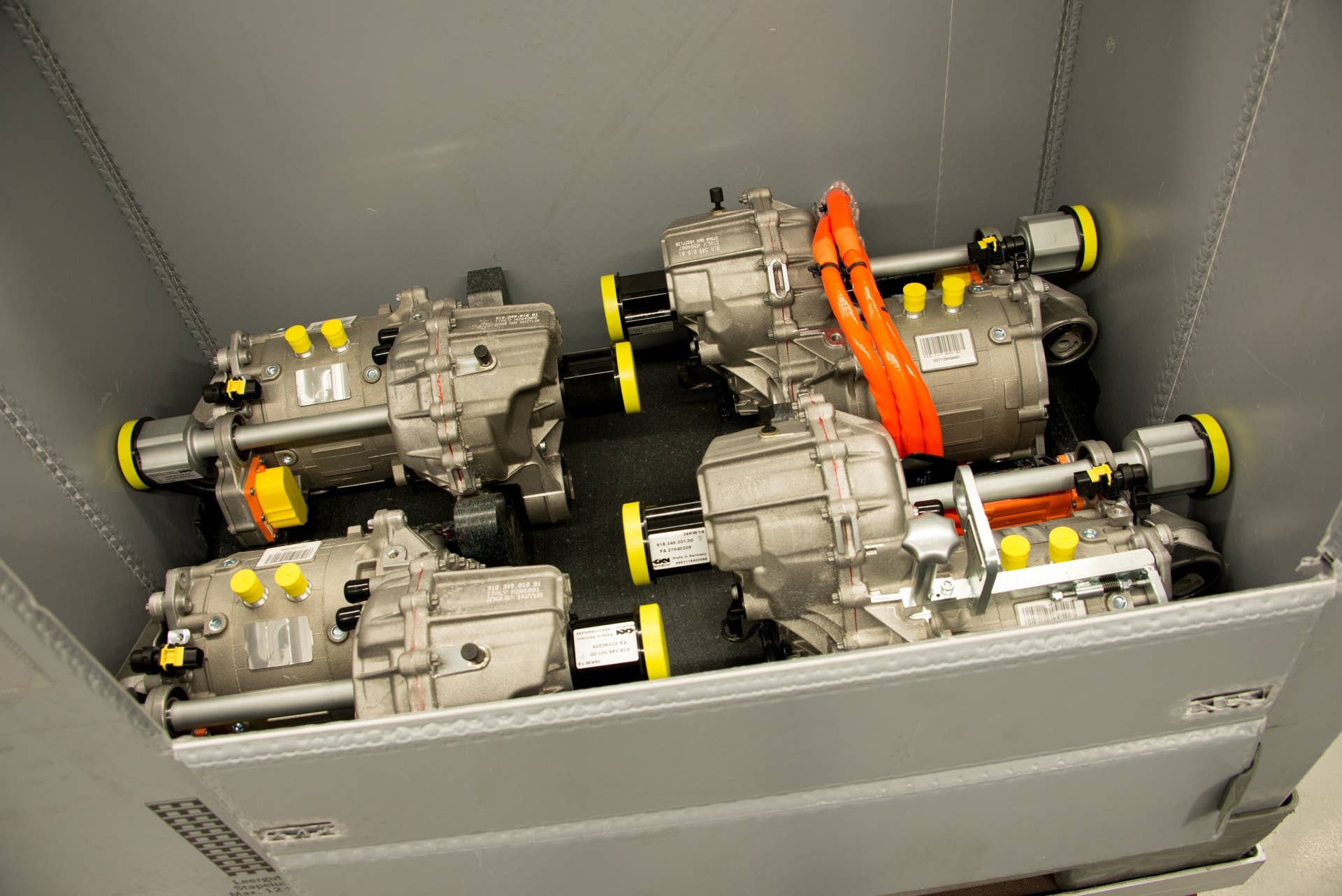 This box contains front drive motors. The axles, connected to the front wheels, will bolt where the yellow bands are at each side while the thick orange cable will hook into the high-voltage hybrid electric system.  Temporary steel hardware (bright silver with a knurled knob at the top) has been attached to the motor in the lower right corner to allow an electric winch to pull it out of the shipping container.