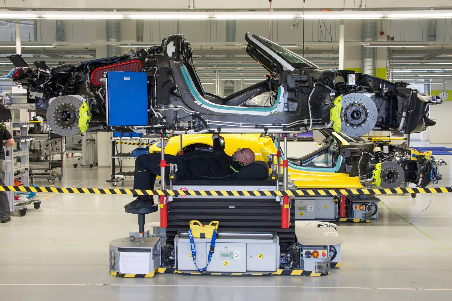 A technician works beneath the 918 chassis, about 75 percent complete at this stage. The engine and battery have been installed, as have the front and rear suspension and steering components.   Aerodynamic panels— most painted, but some not — will cover just about every surface, and restrict access to wiring, cooling lines and motors, so they are the last to be installed.