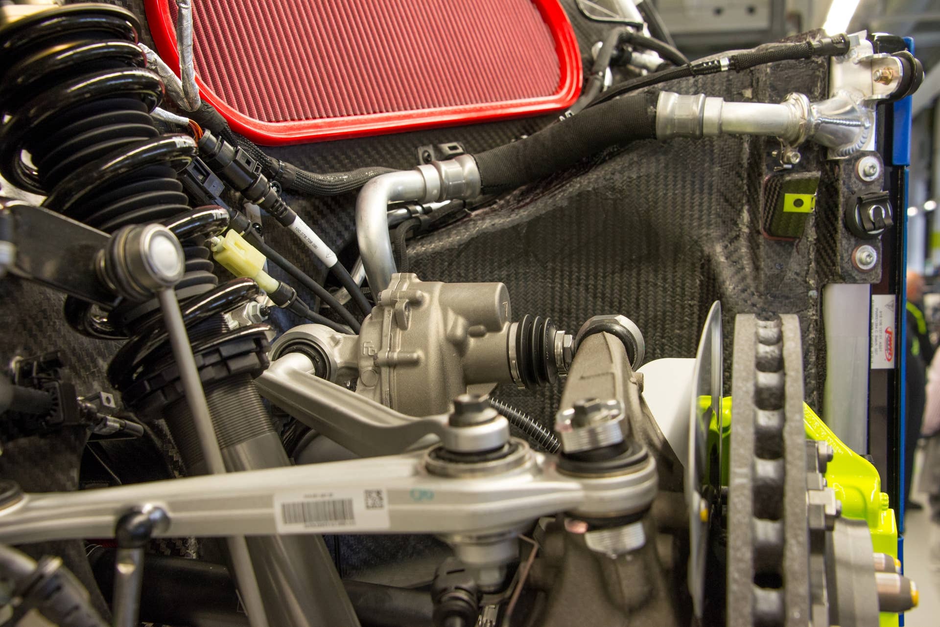 A view from the right rear of the 918, looking over the right rear brake rotor, which shows the motor tasked with moving the rear-wheel steering mechanism. The coil-over suspension is visible to the left of the image. The large red panel at the top is one of two air filters for the combustion engine.