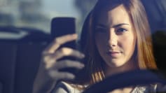 Front view of woman driving and typing on smart phone