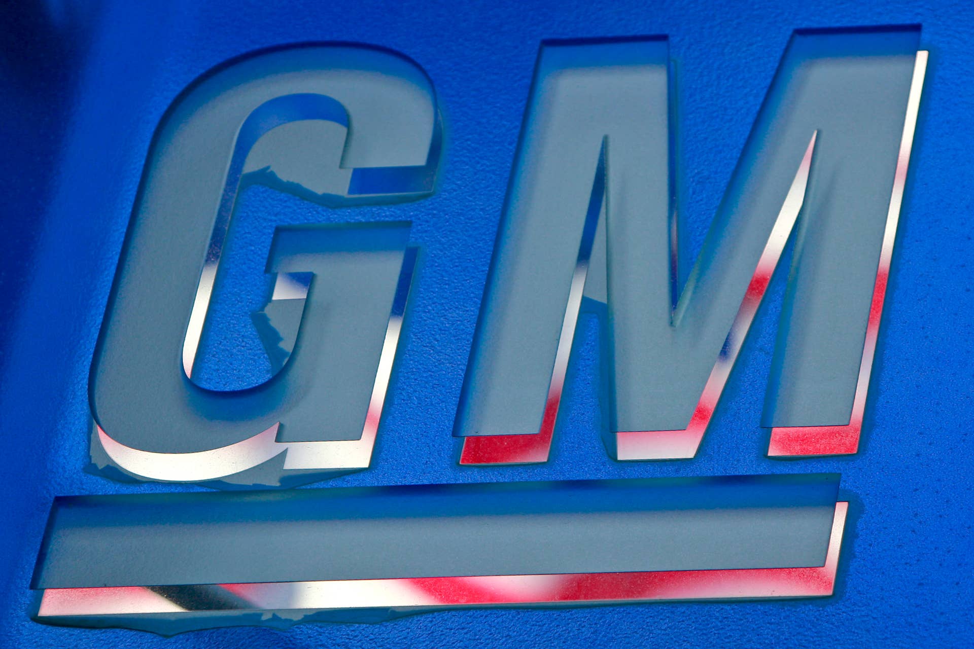 A U.S. flag is reflected in a peeling General Motors Co. logo outside the company's headquarters building in Detroit, Michigan, U.S., on Tuesday, June 1, 2010. General Motors Corp. filed for bankruptcy protection one year ago today, becoming the largest failure of an industrial company in U.S. history. The company, now known as General Motors Co. (GM), is currently seeking to sell shares in an initial public offering. Photographer: Jeff Kowalsky/Bloomberg via Getty Images