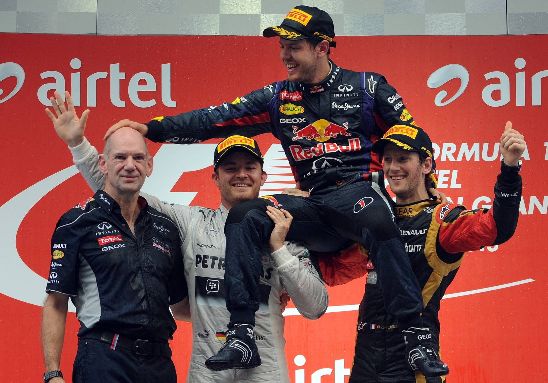 Red Bull driver Sebastian Vettel (C) of Germany hoisted by Mercedes driver Nico Rosberg (2L) of Germany and Lotus driver Romain Grosjean (R) of France pats Red Bull Chief Technical Officer Adrian Newey (L) after winning the Formula One Indian Grand Prix 2013 at the Buddh International circuit in Greater Noida, on the outskirts of New Delhi on October 27, 2013.  AFP PHOTO/Indranil MUKHERJEE        (Photo credit should read INDRANIL MUKHERJEE/AFP/Getty Images)