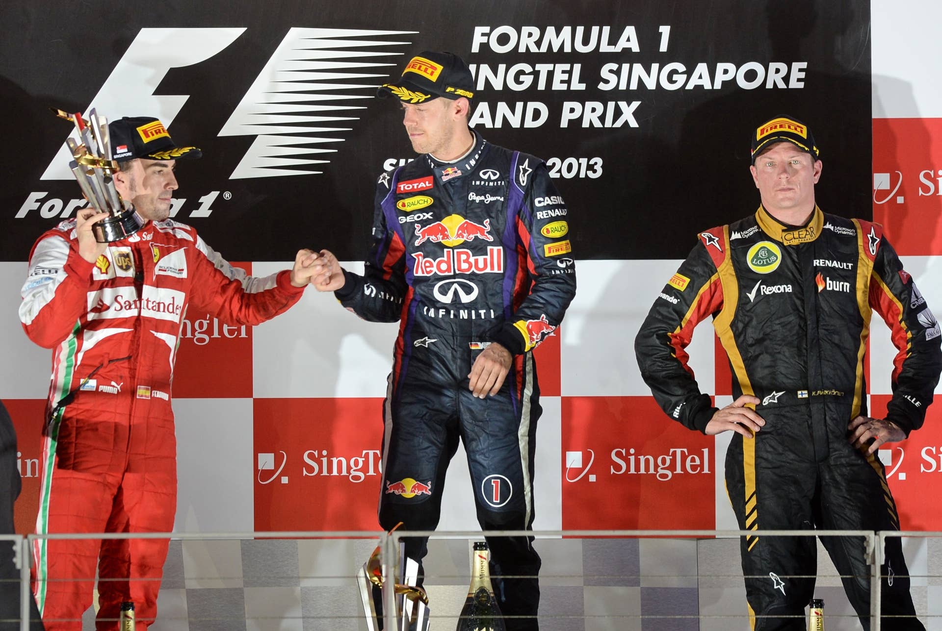 Winner Red Bull driver Sebastian Vettel of Germany (C) greets second-placed Ferrari driver Fernando Alonso of Spain (L) while third-placed Lotus driver Kimi Raikkonen of Finland (R) looks on during the awards ceremon on the podium at the Formula One Singapore Grand Prix on September 22, 2013.     AFP PHOTO / ROSLAN RAHMAN        (Photo credit should read ROSLAN RAHMAN/AFP/Getty Images)