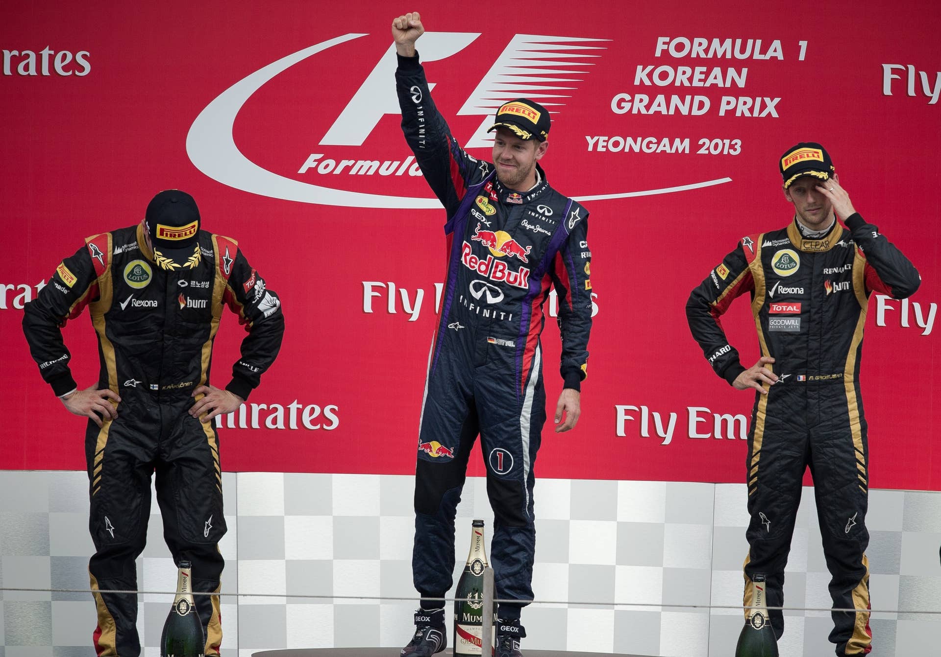 Lotus driver Kimi Raikkonen (L) of Finland and Lotus driver Romain Grosjean (R) of France gesture as Red Bull driver Sebastian Vettel of Germany celebrates after winning the Formula One Korean Grand Prix in Yeongam on October 6, 2013. AFP PHOTO/ Nicolas ASFOURI        (Photo credit should read NICOLAS ASFOURI/AFP/Getty Images)