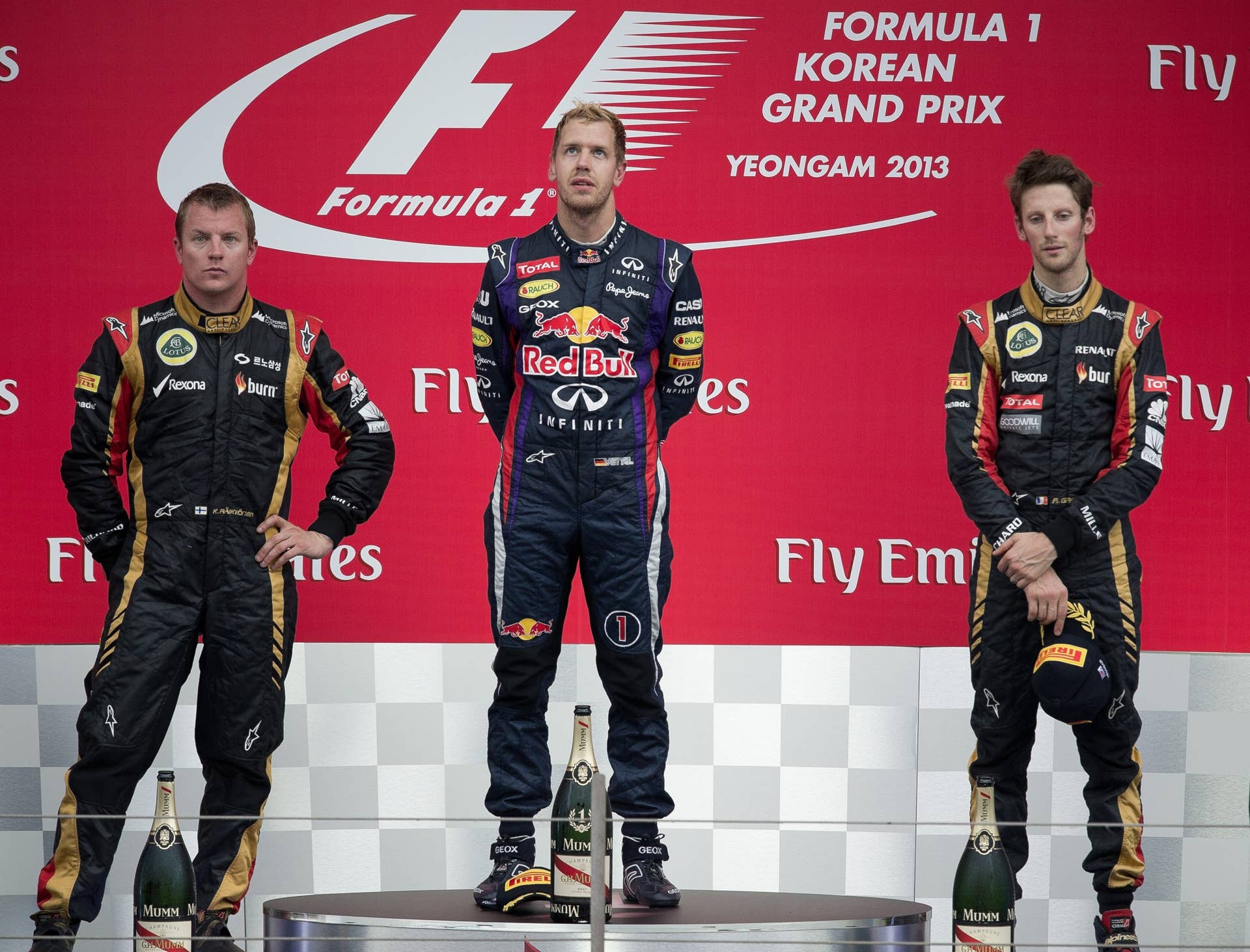 Lotus driver Kimi Raikkonen (L) of Finland, Lotus driver Romain Grosjean (R) of France and Red Bull driver Sebastian Vettel of Germany listen to the German national anthem after Vettel won the Formula One Korean Grand Prix in Yeongam on October 6, 2013. AFP PHOTO/ Nicolas ASFOURI        (Photo credit should read NICOLAS ASFOURI/AFP/Getty Images)