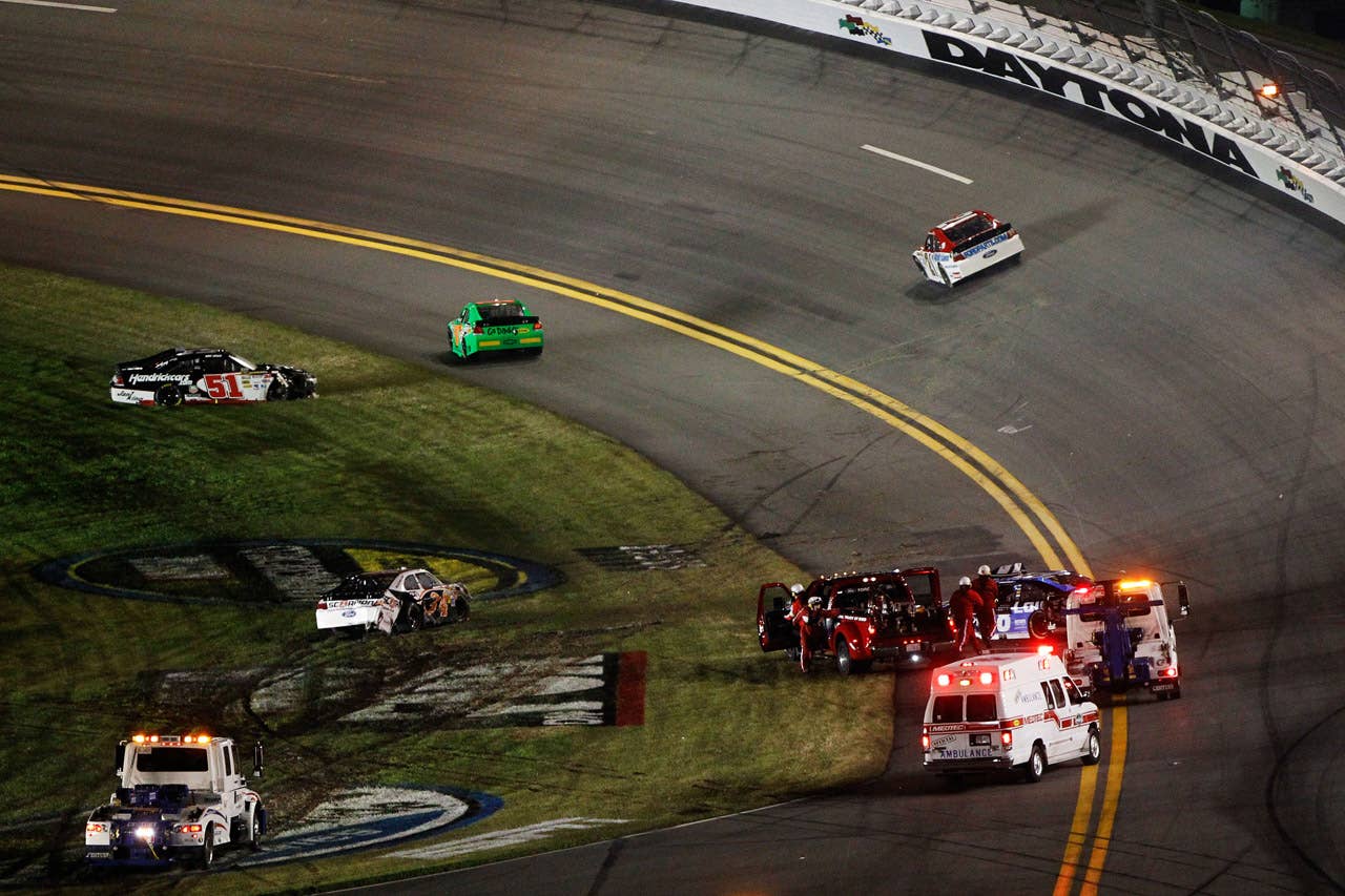 DAYTONA BEACH, FL - FEBRUARY 27:  Safety workers tend to Jimmie Johnson, driver of the #48 Lowe's Chevrolet, as Dave Blaney, driver of the #36 Ollie's Bargain Outlet Chevrolet, and Kurt Busch, driver of the #51 Tag Heuer Avant-Garde Chevrolet Chevrolet, sit in the grass after an on track incident during the NASCAR Sprint Cup Series Daytona 500 at Daytona International Speedway on February 27, 2012 in Daytona Beach, Florida.  (Photo by Tom Pennington/Getty Images for NASCAR)