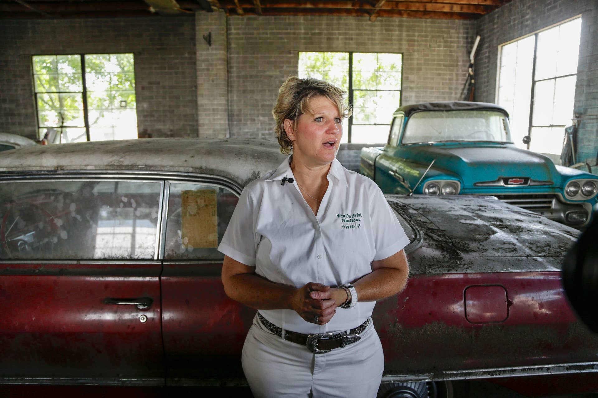 In this Aug. 12, 2013 photo, auctioneer Yvette VanDerBrink stands in front of a brand new, old 1963 Chevrolet Impala and a brand new, old 1958 Cameo pickup truck, right, at the former Lambrecht Chevrolet car dealership in Pierce, Neb. Next month, bidders from at least a dozen countries and all 50 U.S. states will converge on Pierce, a town of about 1,800 in northeast Nebraska, for a two-day auction that will feature about 500 old cars and trucks, mostly Chevrolets that went unsold during the dealership?s five decades in business. About 50 have fewer than 20 miles on the odometer, and some are so rare that no one has established a price. The most valuable could fetch six-figure bids. (AP Photo/Nati Harnik)