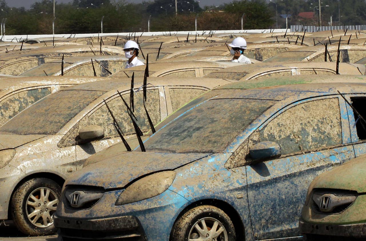Workers walk amidst Honda cars that were damaged by the flood before the destruction demonstration at Honda automobile plant in Ayutthaya province, central Thailand Tuesday, Dec. 27, 2011. The 1,055 unit of Honda cars, mostly Brio eco-cars and City subcompacts, were destroyed in an action to assure to customers that the flood-damaged cars will not be repaired and sold. (AP Photo/Apichart Weerawong)