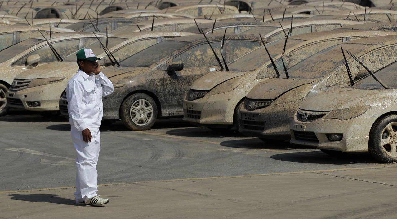 A worker talks on his mobile phone next to lines of Honda cars that were damaged by the flood before the destruction demonstration at Honda automobile plant in Ayutthaya province, central Thailand Tuesday, Dec. 27, 2011. The 1,055 unit of Honda cars, mostly Brio eco-cars and City subcompacts, were destroyed in an action to assure to customers that the flood-damaged cars will not be repaired and sold. (AP Photo/Apichart Weerawong)