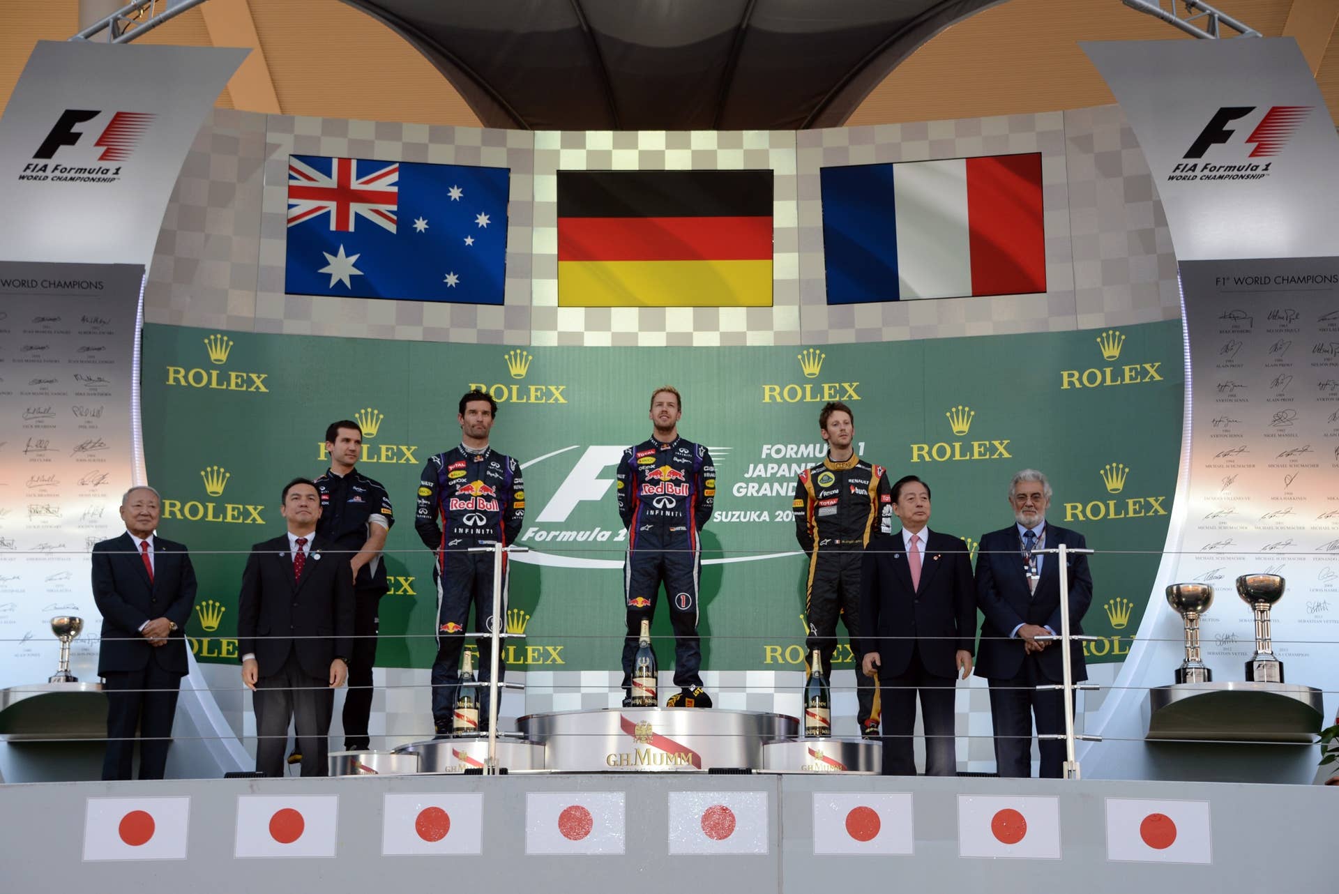 Winning Red Bull driver Sebastian Vettel of Germany (C) listens to the national anthem on the podium with second placed Red Bull driver Mark Webber of Australia (4th L) and third placed Lotus driver Romain Grosjean of France (3rd R) during the Formula One Japanese Grand Prix in Suzuka on October 13, 2013.    AFP PHOTO / TOSHIFUMI KITAMURA        (Photo credit should read TOSHIFUMI KITAMURA/AFP/Getty Images)
