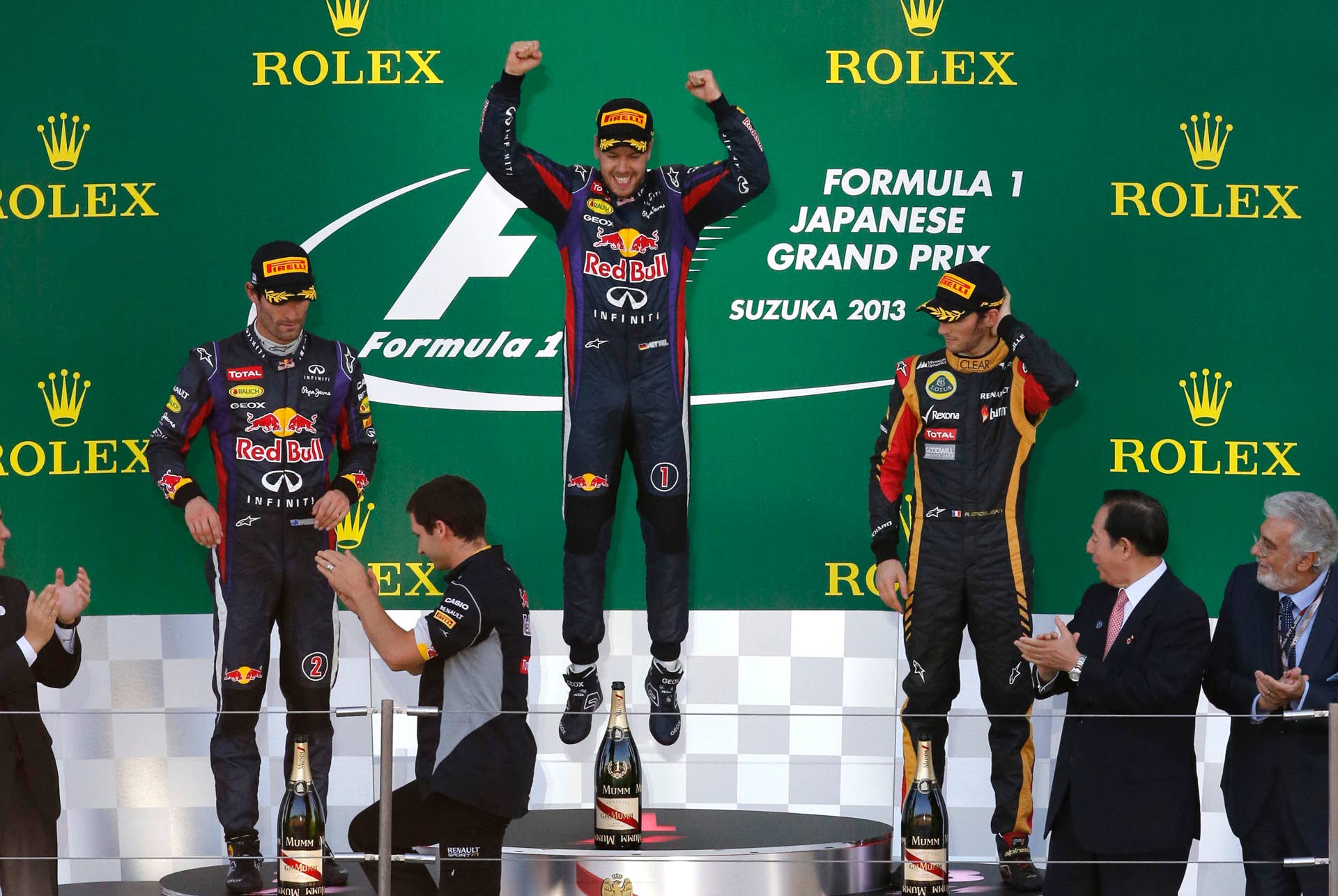 Red Bull driver Sebastian Vettel of Germany, center,  jumps on the podium as he celebrates after winning the Japanese Formula One Grand Prix at the Suzuka circuit in Suzuka, Japan, Sunday, Oct.13, 2013. At left is second placed Red Bull driver Mark Webber of Australia and third placed Lotus driver Romain Grosjean of France at right. (AP Photo/Shuji Kajiyama)