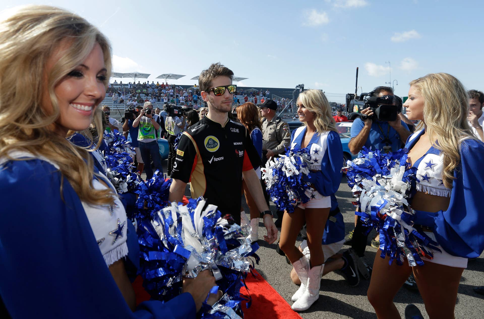 Lotus driver Romain Grosjean of Switzerland walks past the Dallas Cowboy cheerleaders before the Formula One U.S. Grand Prix auto race at the Circuit of the Americas, Sunday, Nov. 17, 2013, in Austin, Texas. (AP Photo/Darron Cummings)