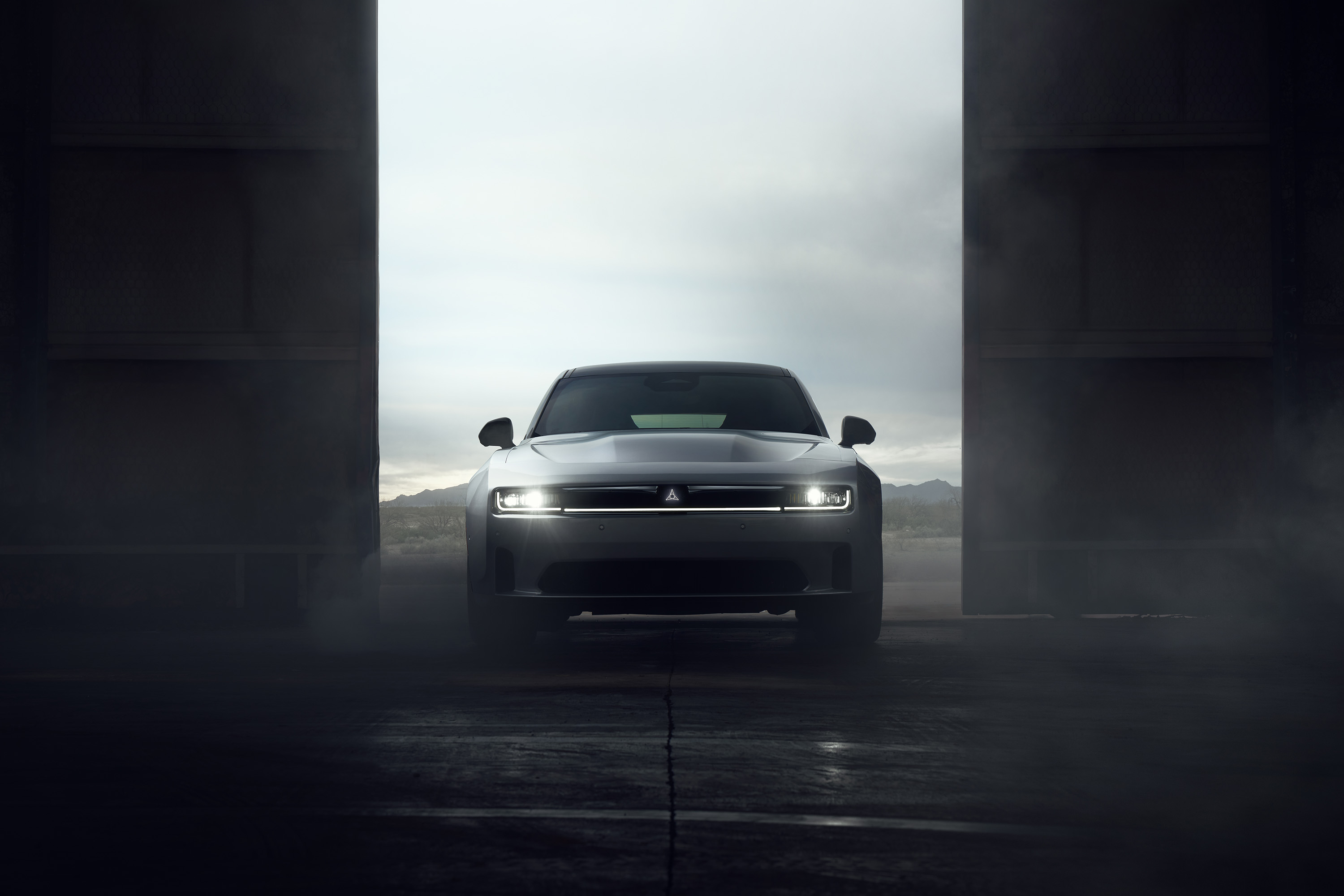 Front view of a 2024 Dodge Charger EV Daytona Scat Pack emerging through hangar doors