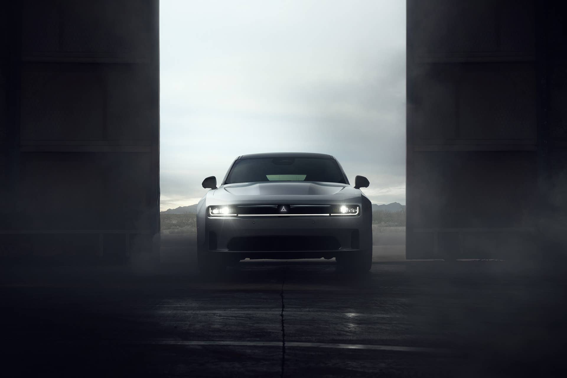 Front view of a 2024 Dodge Charger EV Daytona Scat Pack emerging through hangar doors