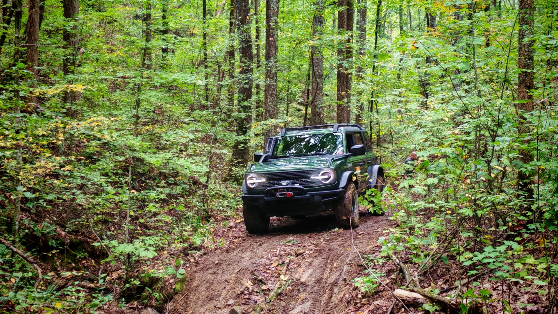 A green Ford Bronco about to descend a muddy slope