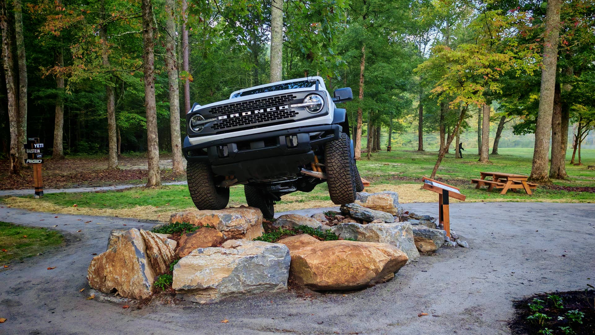 A white Ford Bronco on a rocky plinth with two wheels in the air