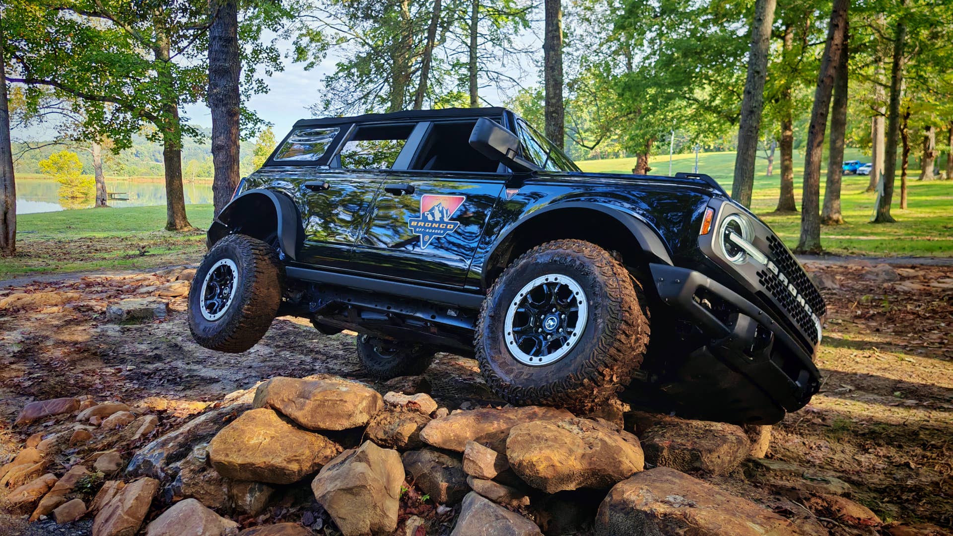 A black Ford Bronco climbing over rocks with its back wheel in the air