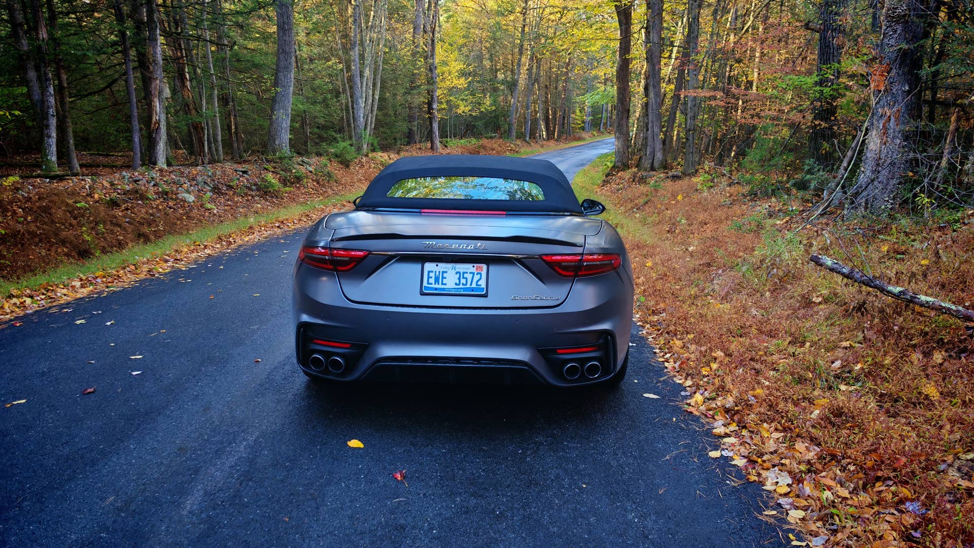 The rear of a Maserati GranCabrio in grey on a leaf strewn woodland road