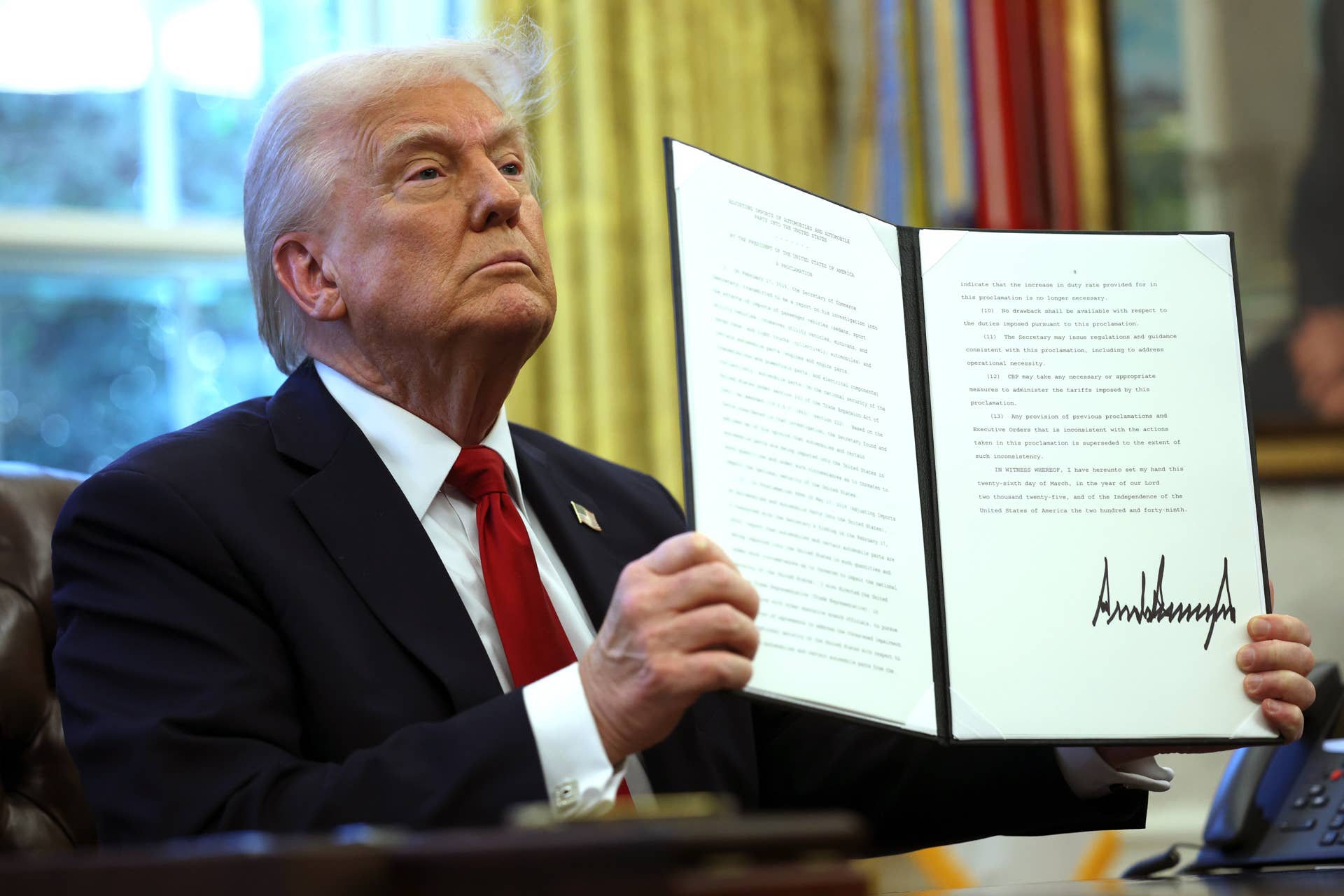 U.S. President Donald Trump displays a signed an executive order in the Oval Office of the White House on March 26, 2025 in Washington, DC.