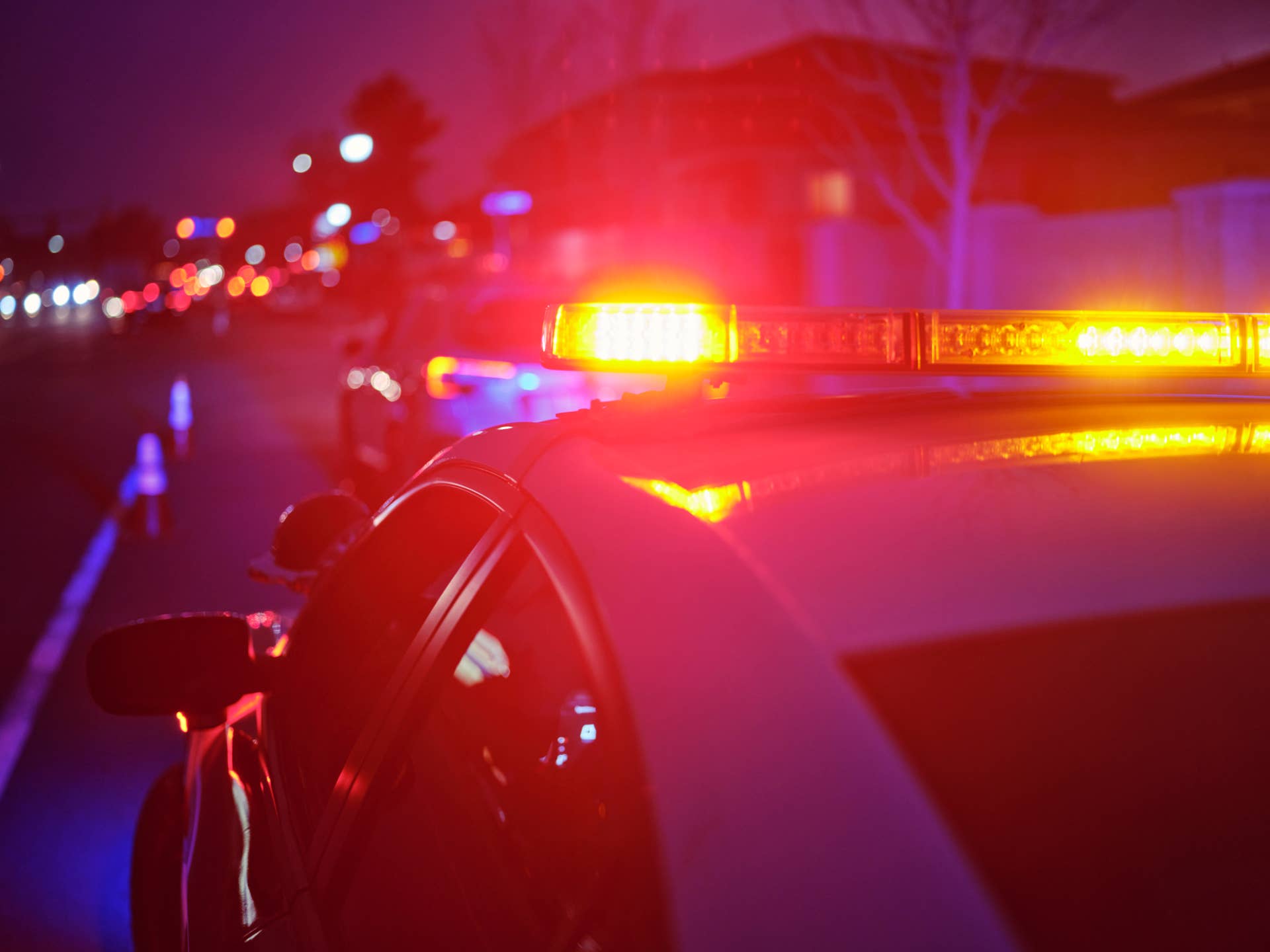 A police car at night alongside a road with emergency lights flashing
