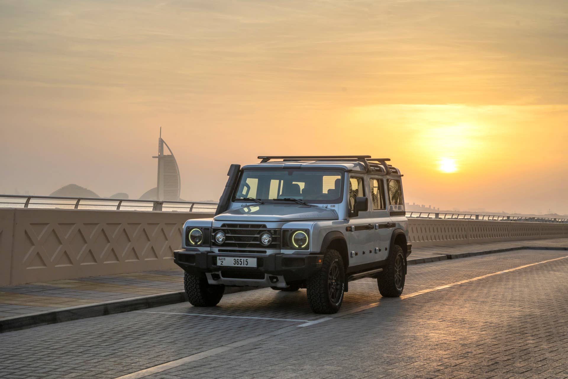 Ineos Grenadier on a bridge, with sunset behind it.