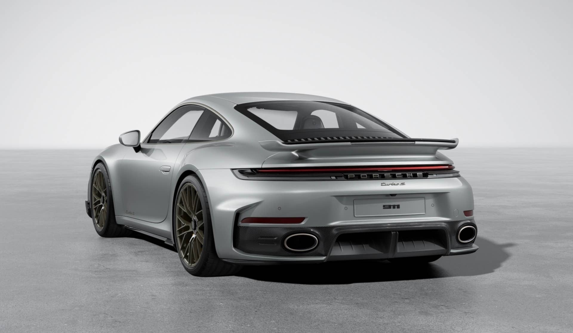 2026 Porsche 911 Turbo S with SportDesign package in carbon fiber silver rear angled view