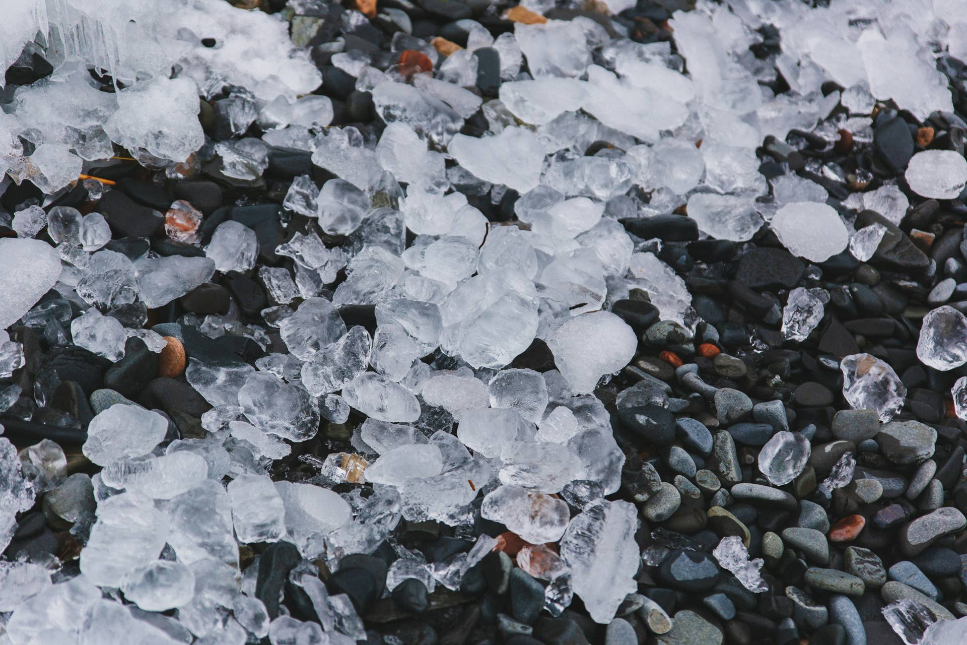 Large chunks of ice and hailstones scattered across wet pebbles and rocks after a severe hailstorm
