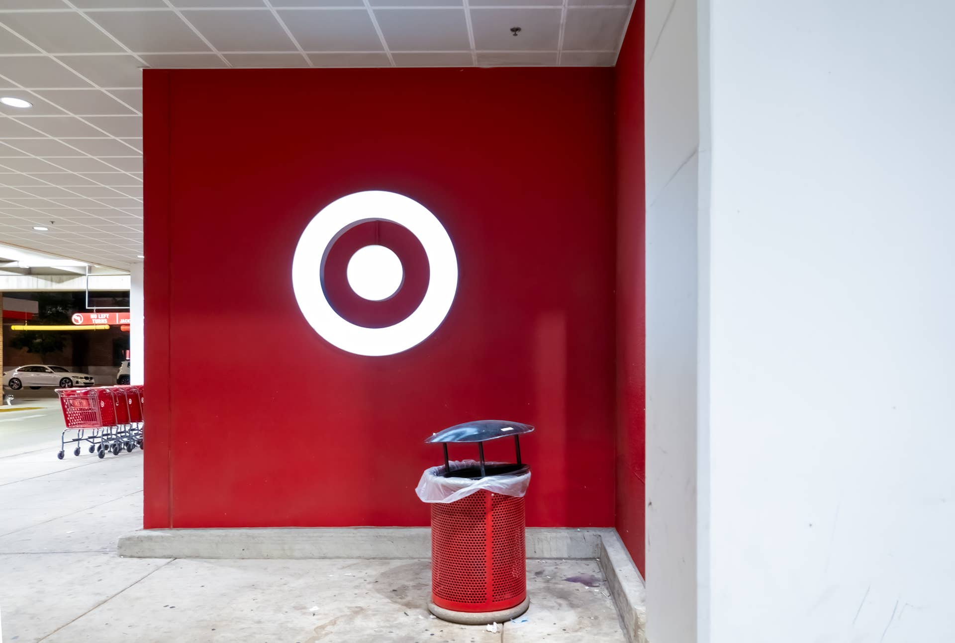 Chicago, Illinois, USA - The illuminated white Target bullseye logo on a red wall, next to a matching red trash can, with shopping carts in background.