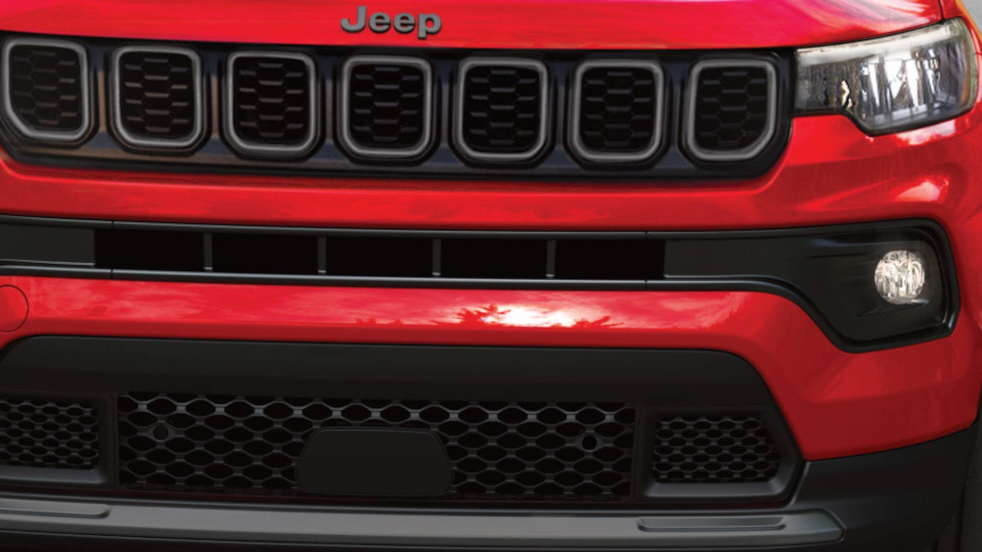 2027 Jeep® Compass Limited Altitude in Red Hot Pearl driving on tree lined road with cloudy skies and hills visible in the distance.