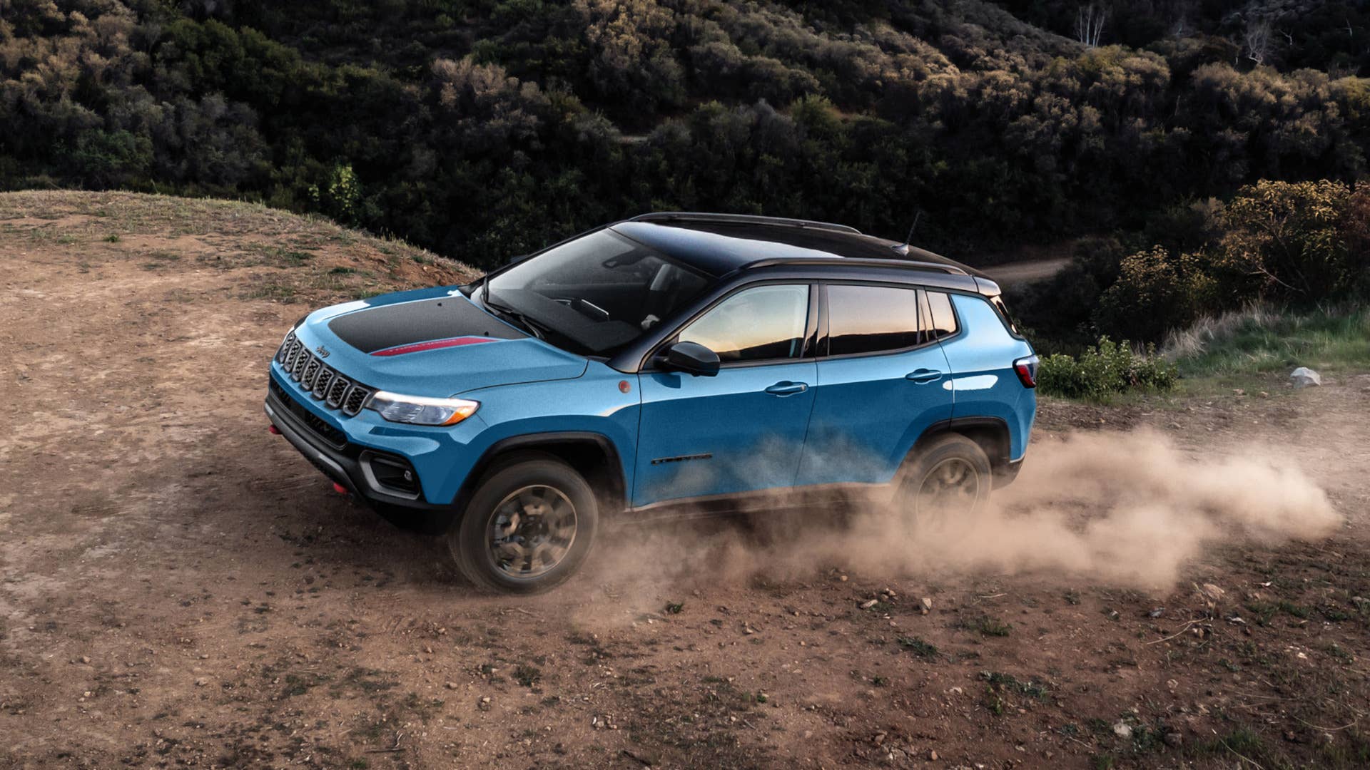 2027 Jeep® Compass Trailhawk in Hydro Blue Pearl driving up a dusty dirt road through the hills.