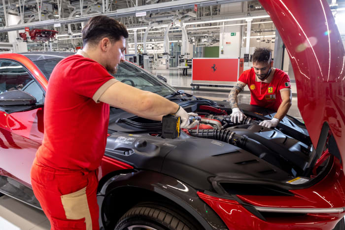 Factory workers wield pneumatic tools to help mate a Ferrari engine to its body.