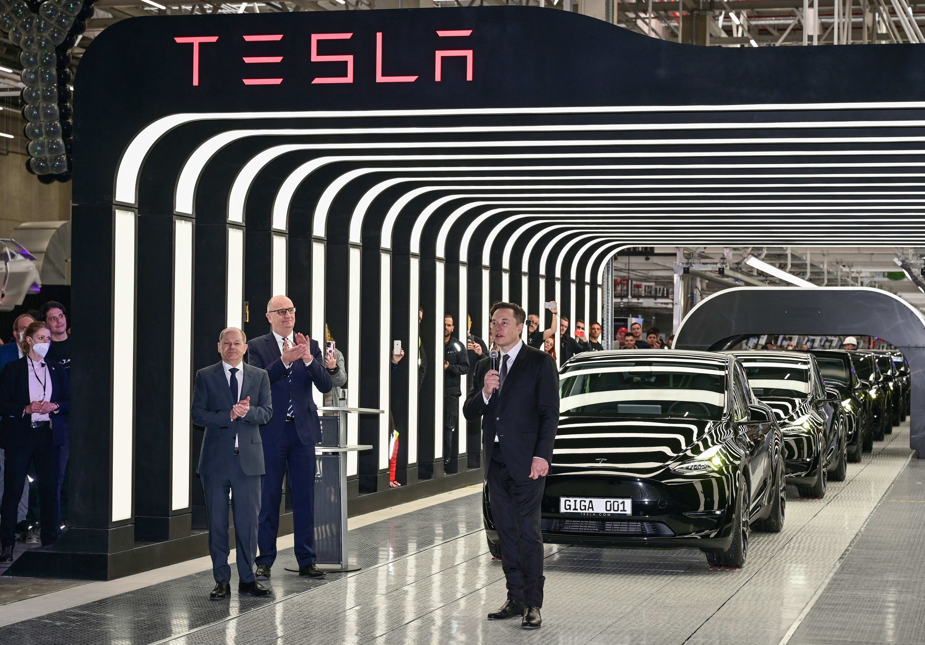 Tesla CEO Elon Musk (R), German Chancellor Olaf Scholz (L) and Brandenburg State Premier Dietmar Woidke applaud as they attend the start of the production at Tesla's "Gigafactory" on March 22, 2022 in Gruenheide, southeast of Berlin. - US electric car pioneer Tesla received the go-ahead for its "gigafactory" in Germany on March 4, 2022, paving the way for production to begin shortly after an approval process dogged by delays and setbacks. (Photo by Patrick Pleul / POOL / AFP) (Photo by PATRICK PLEUL/POOL/AFP via Getty Images)